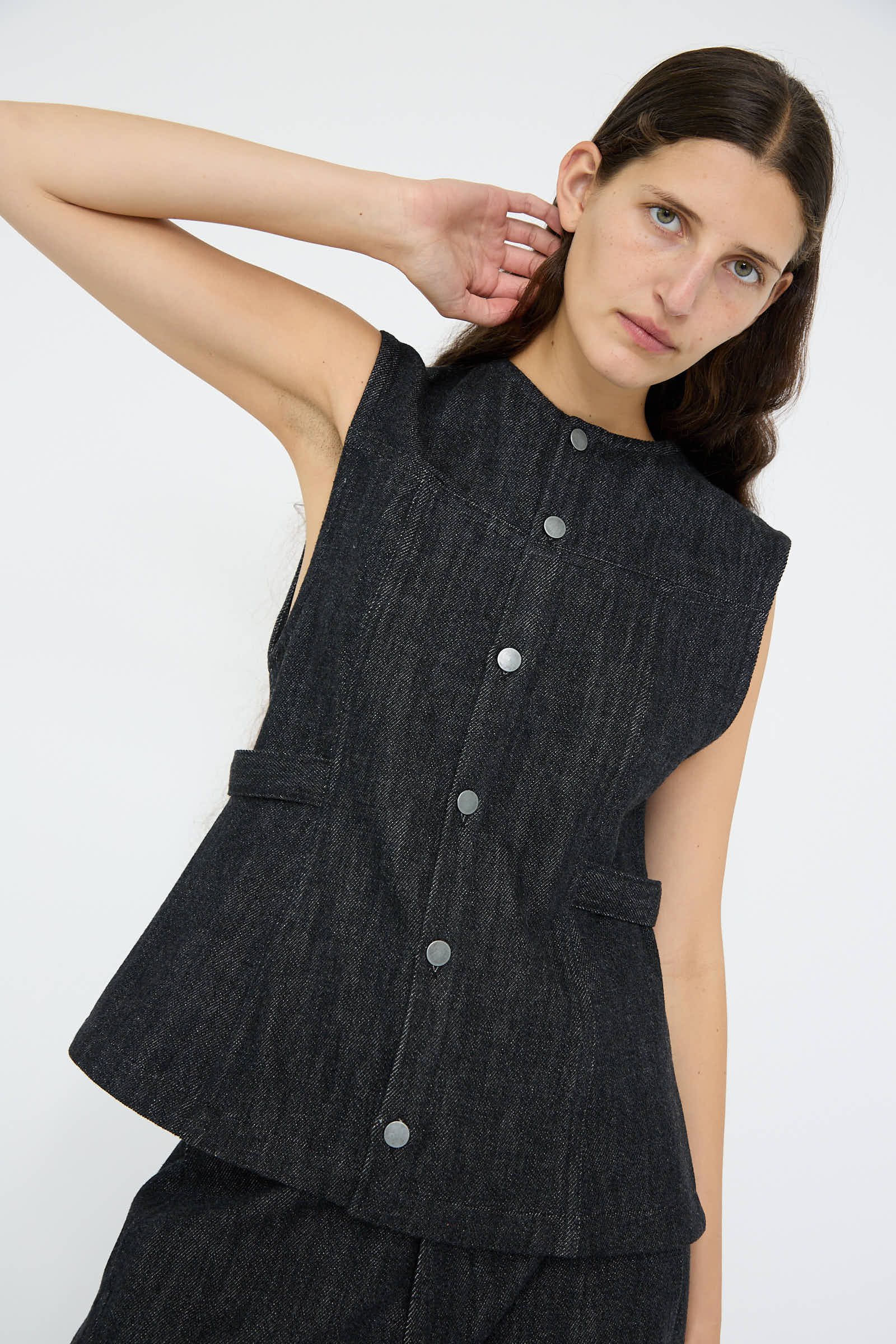 Clad in the Lauren Manoogian Denim Bodice in Indigo, complete with matching 100% cotton pants, the person stands against a plain background while tilting their head with a hand behind their neck.