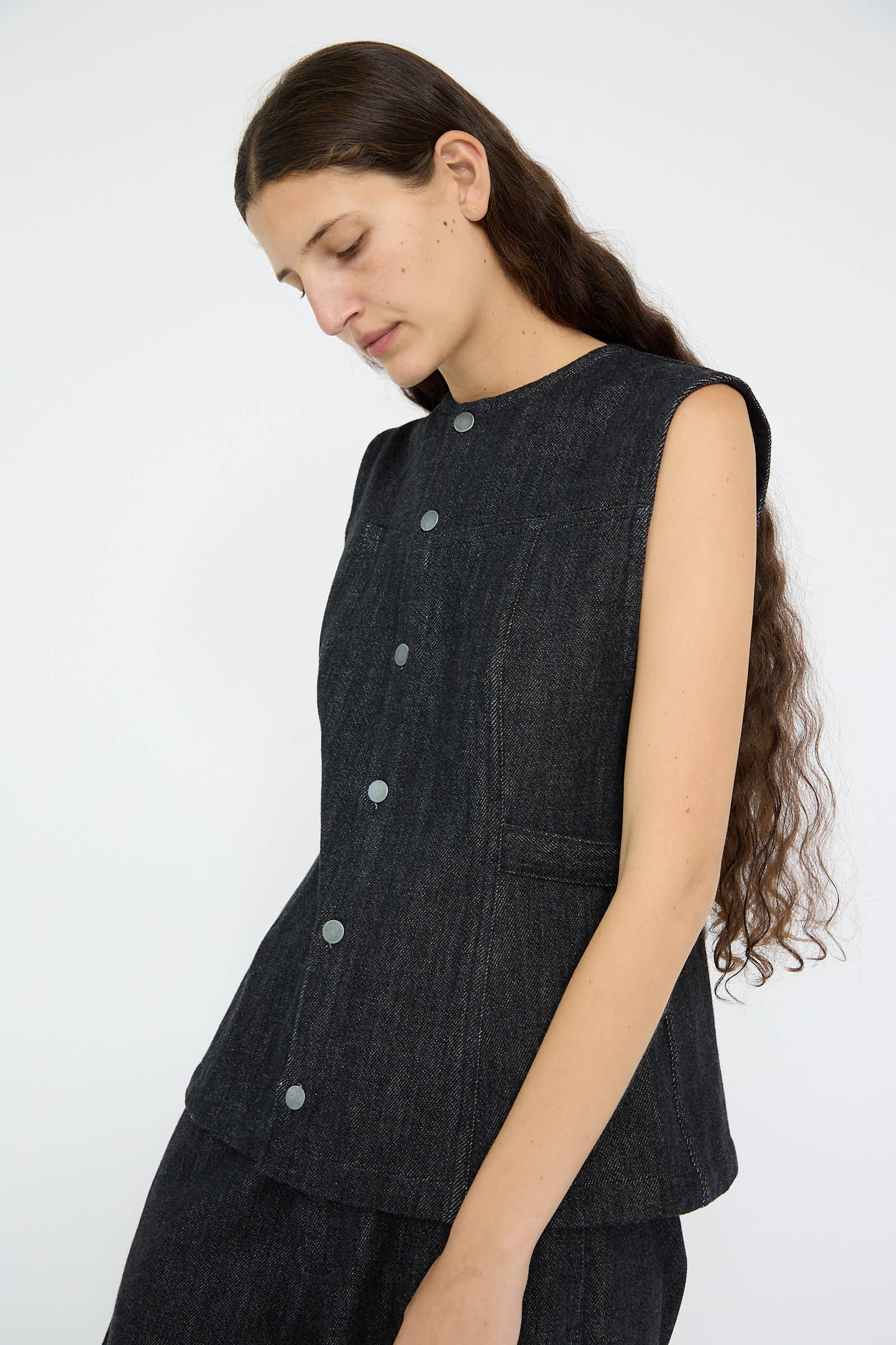 A person with long hair wearing the Sleeveless Denim Bodice in Indigo by Lauren Manoogian, crafted from 100% cotton, stands against a plain white background.