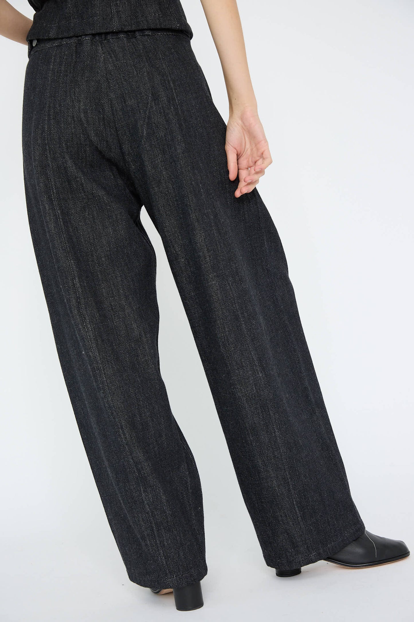 A person wearing the Lauren Manoogian Denim Pant in Indigo, which features a high waist and wide-leg design with an adjustable waist, stands in black shoes in a neutral pose against a white background.