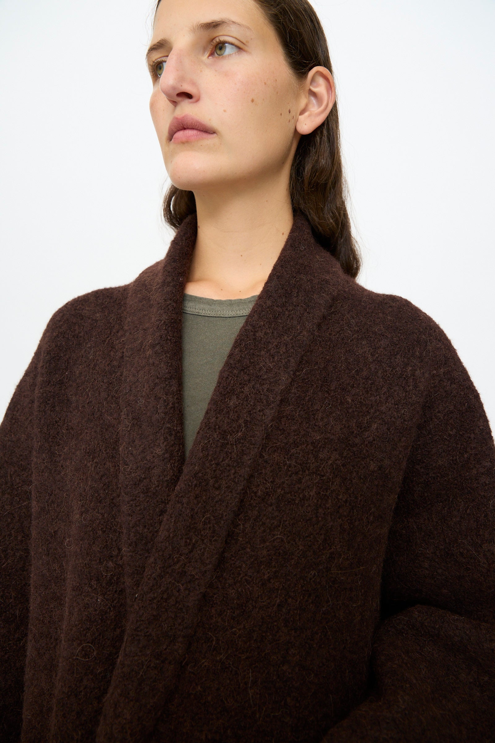 A woman with straight brown hair wears the Lauren Manoogian Double Face Long Coat in Merlot over a green top, standing against a plain light background.