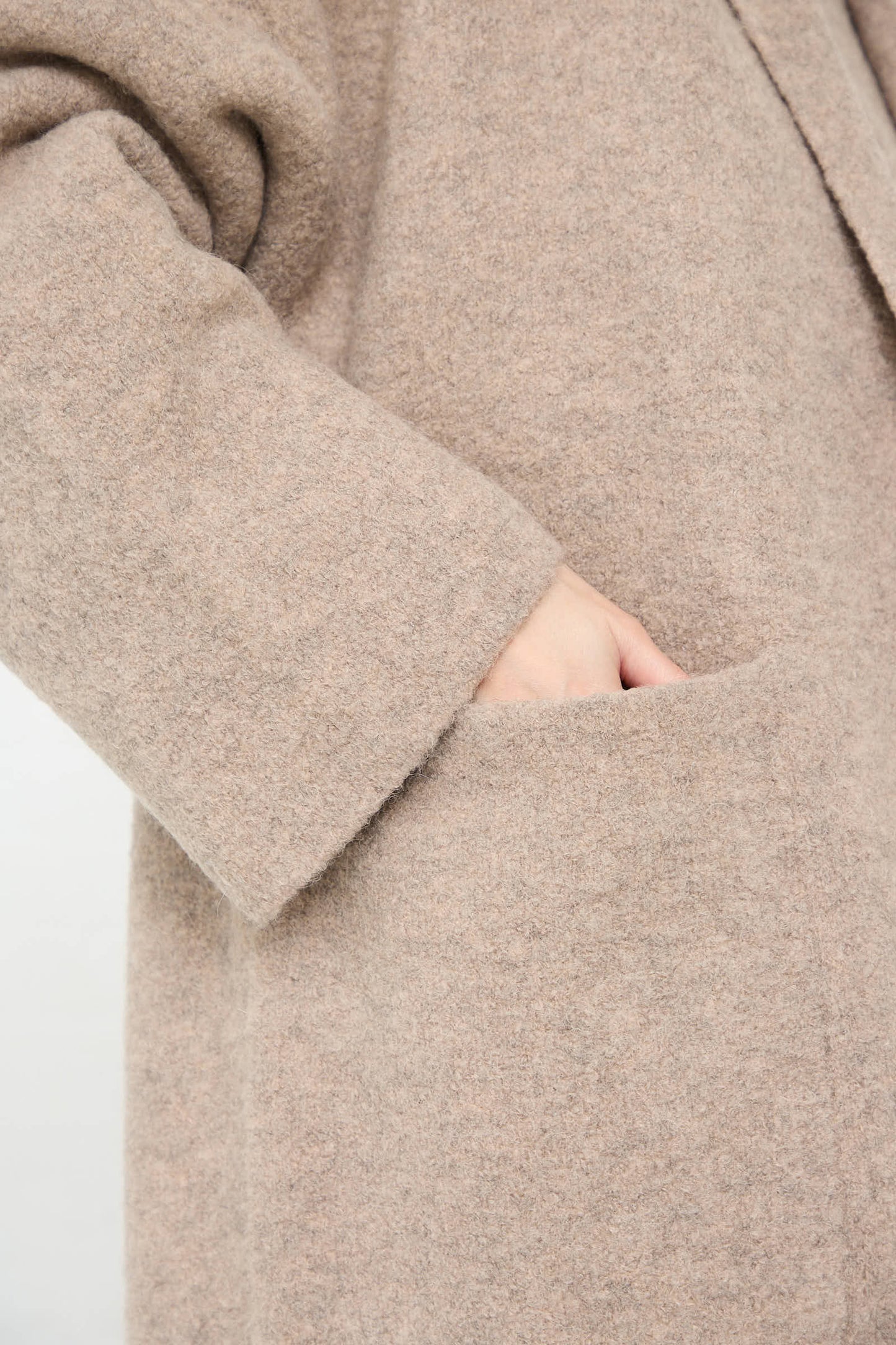 A close-up of a person wearing the Lauren Manoogian Double Face Long Coat in Moth with oversized patch pockets, their hand tucked into one of the cozy compartments.