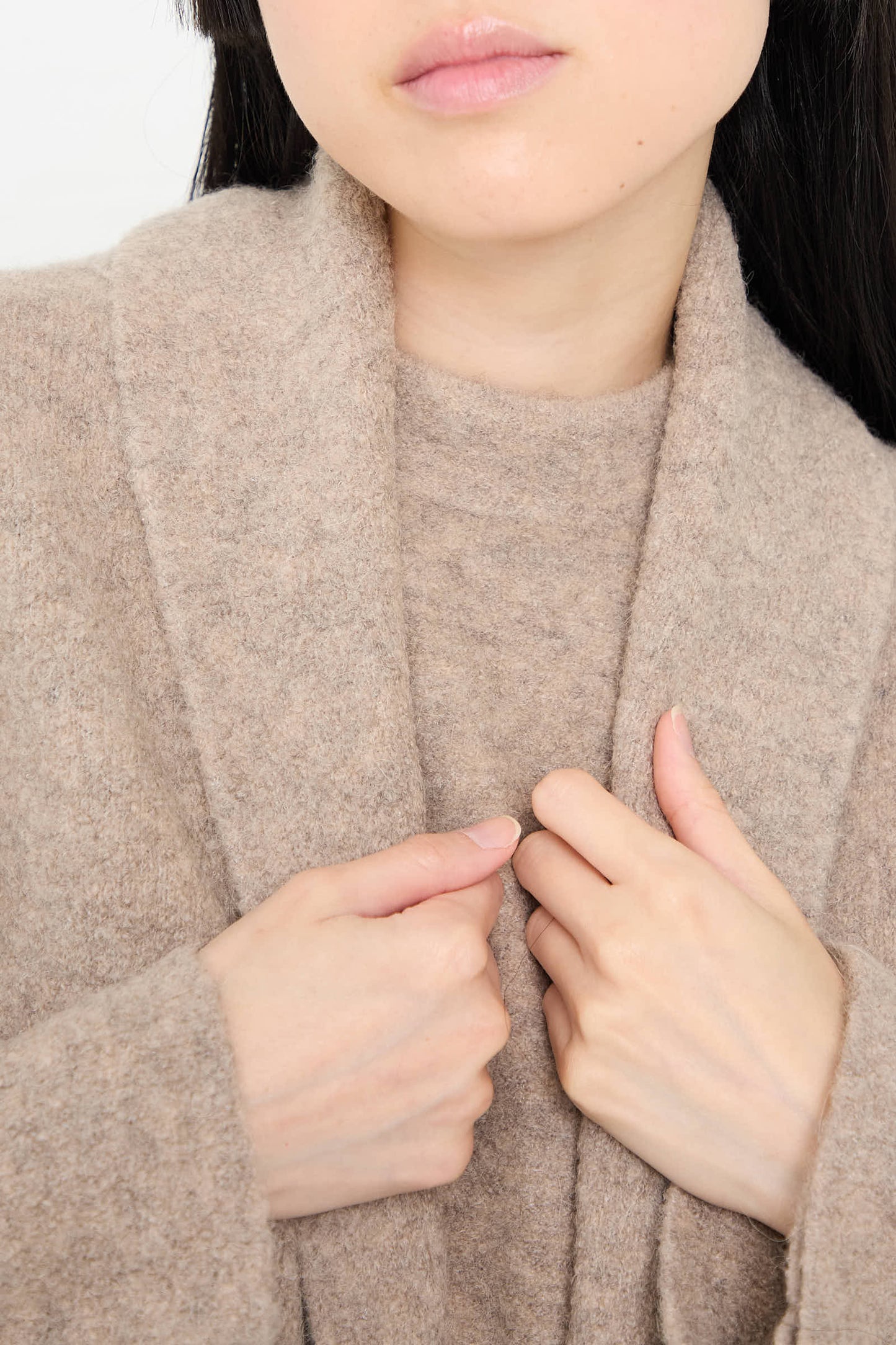 Close-up of a person adjusting the collar of a Double Face Long Coat in Moth by Lauren Manoogian, showing partial face and hands.