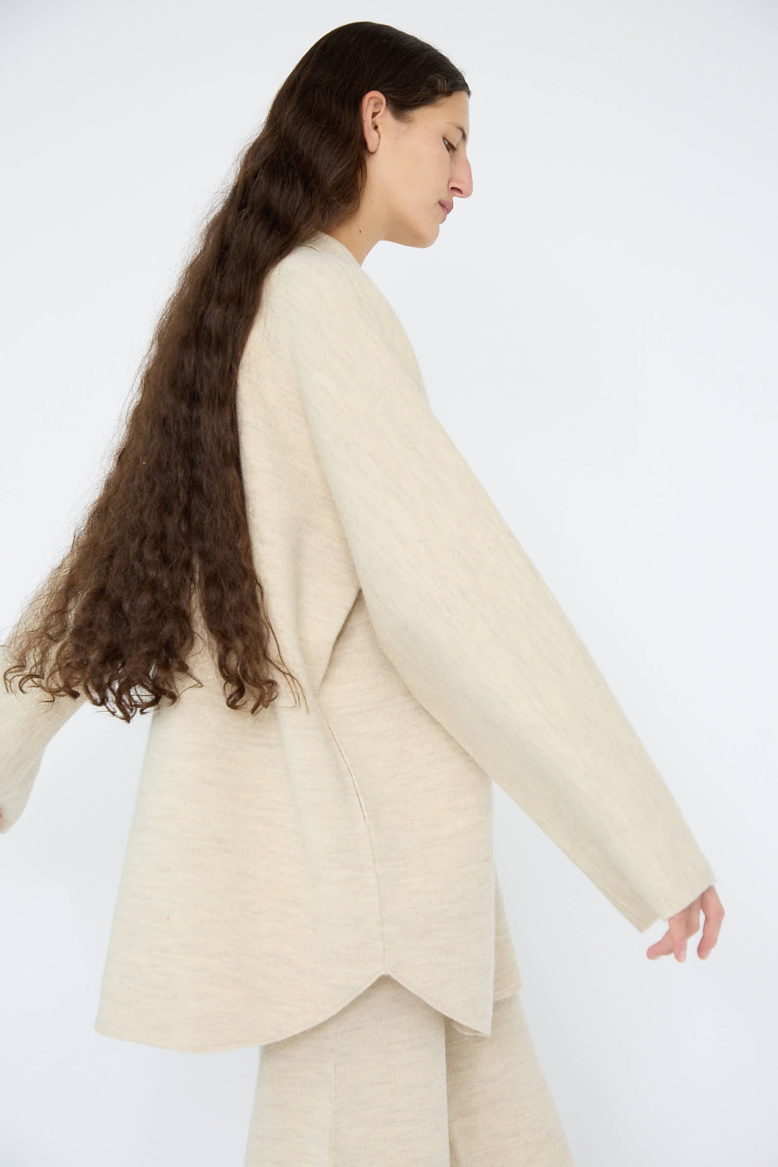 A person with long, brown hair is seen wearing the Lauren Manoogian Double Knit Big Shirt in Ecru, crafted from a wool/alpaca/cotton blend, viewed from the side against a plain white background.