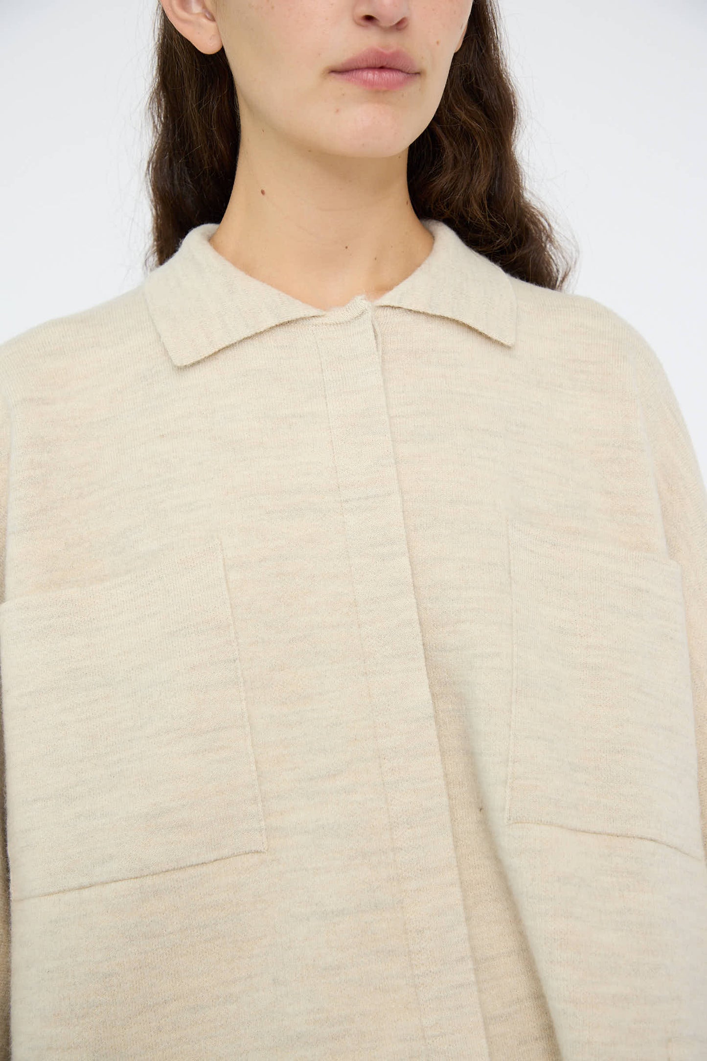 A person is wearing the Double Knit Big Shirt in Ecru by Lauren Manoogian, an oversized light beige collared shirt with two front pockets. This cotton blend piece, crafted in Peru, highlights the upper part of their body.