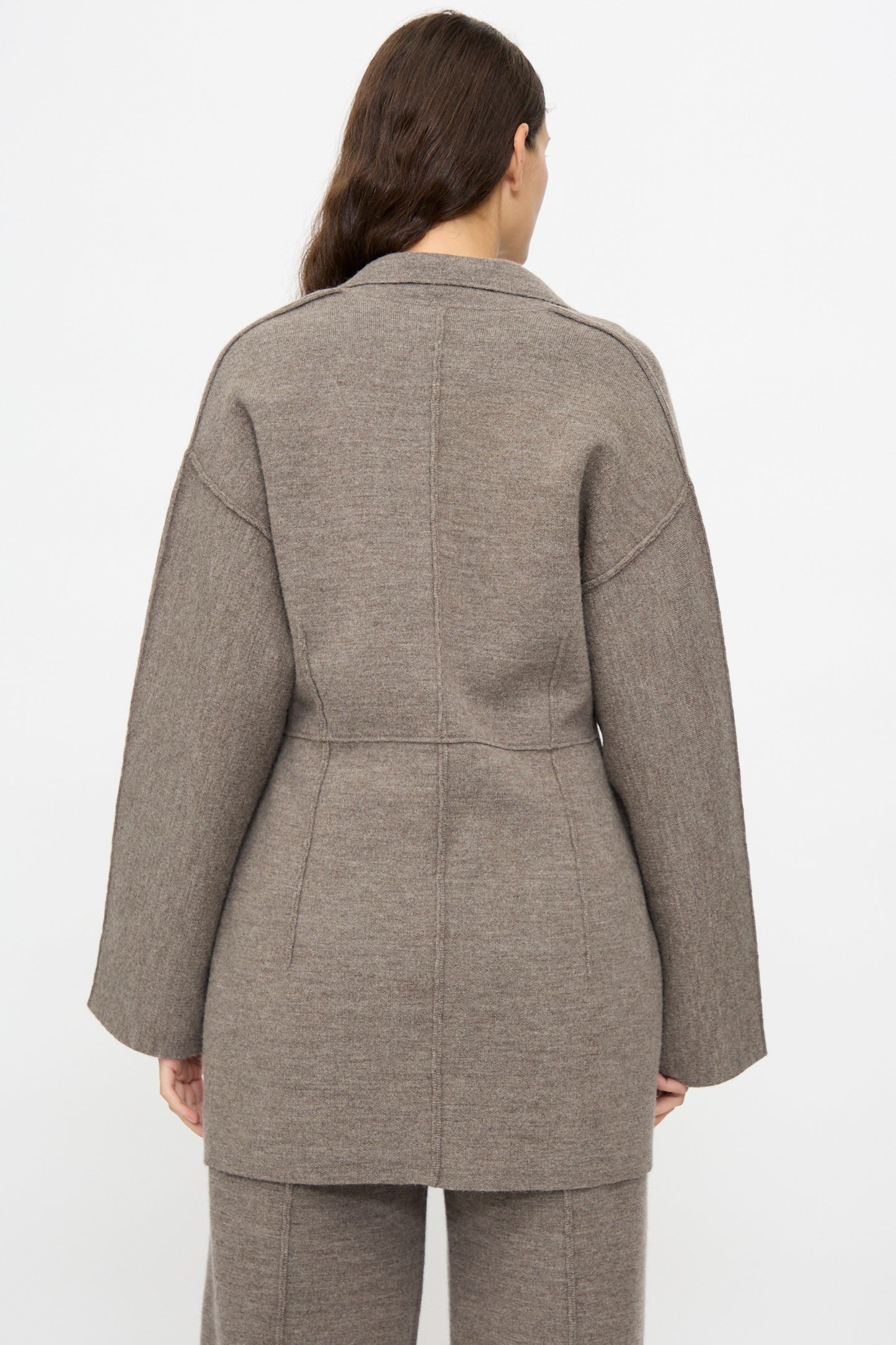 A person with long brown hair is shown from the back, wearing the Lauren Manoogian Double Knit Blazer in Cinder with matching pants against a plain light background.