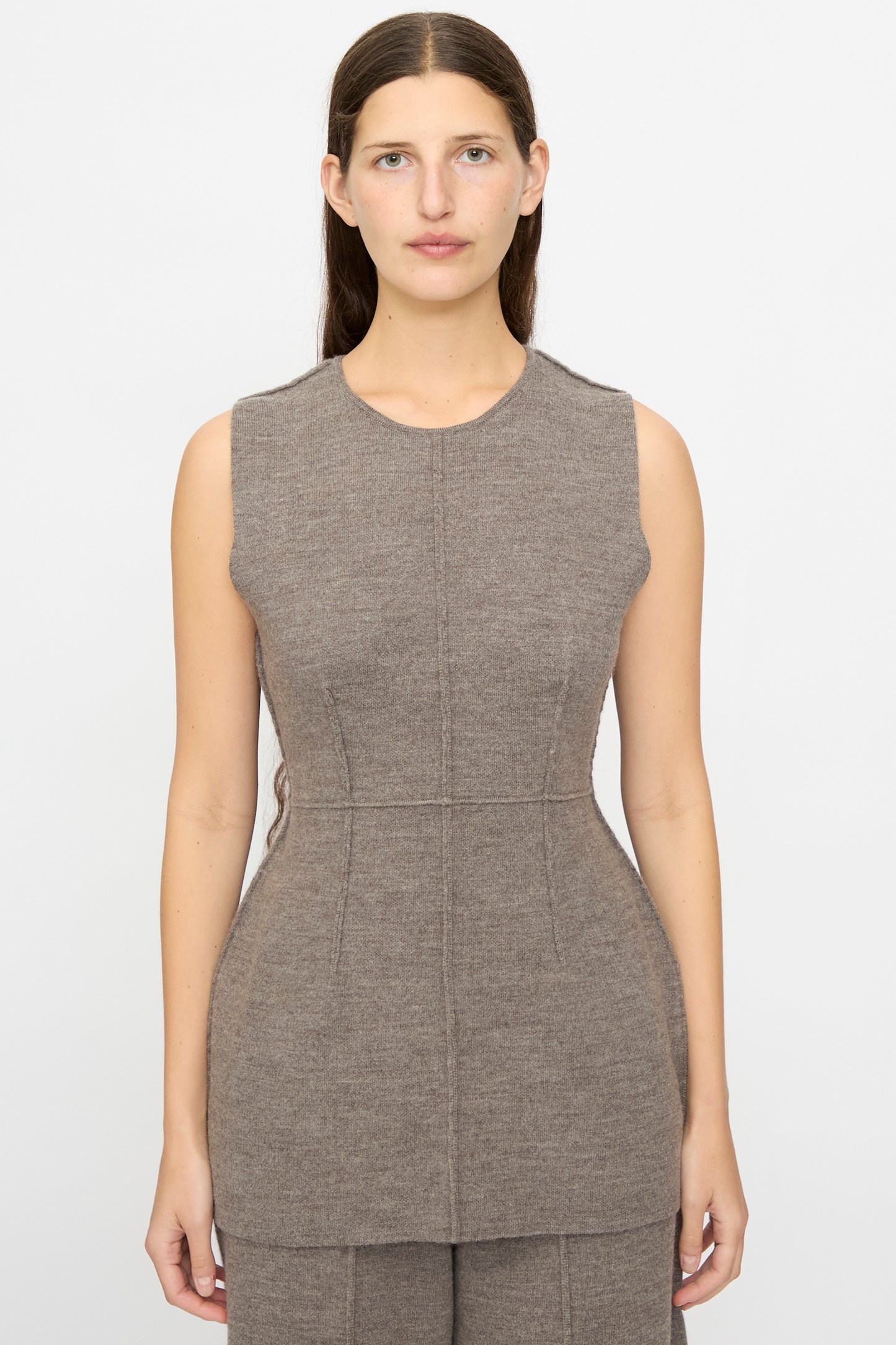 A woman faces forward, wearing the Lauren Manoogian Double Knit Bodice in Cinder—a sleeveless, fitted baby alpaca top with visible seam lines. Her straight hair is worn down, and she stands against a plain white background.