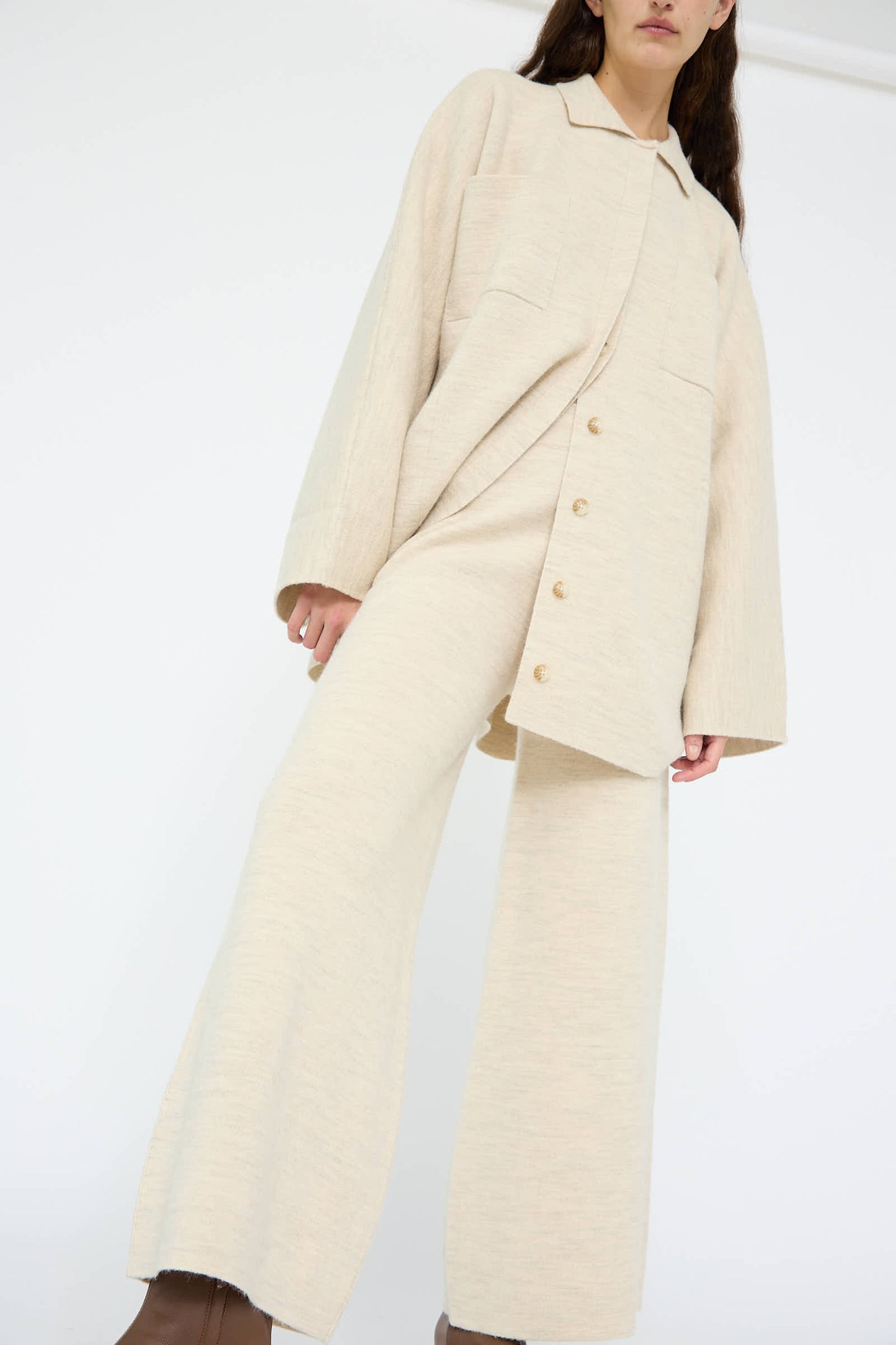 A person wearing a beige oversized button-up top and Lauren Manoogian's Double Knit Flare Pant in Ecru, photographed from a low angle against a plain background.