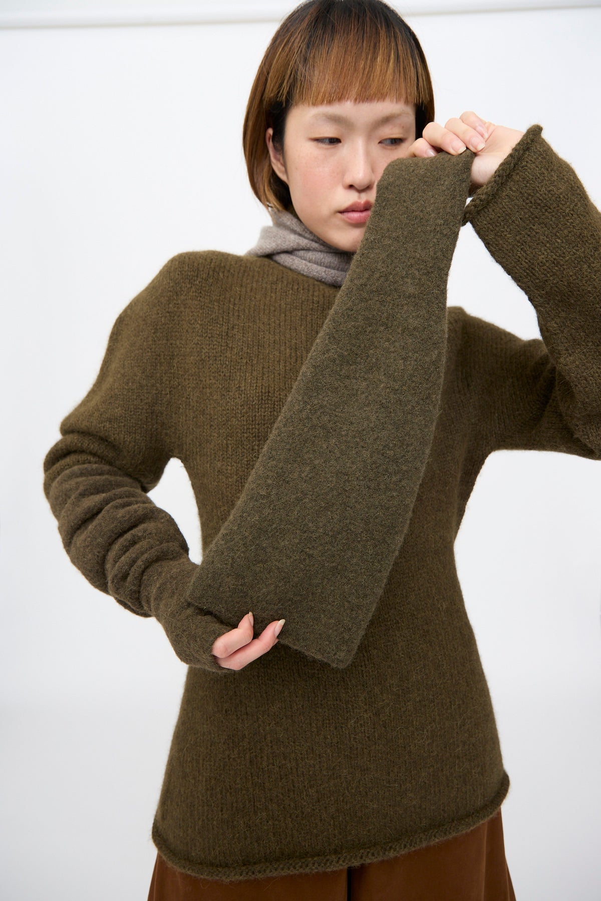 A person wearing an olive green baby alpaca blend knit sweater and a matching Lauren Manoogian Felt Fingerless Glove in Olive.