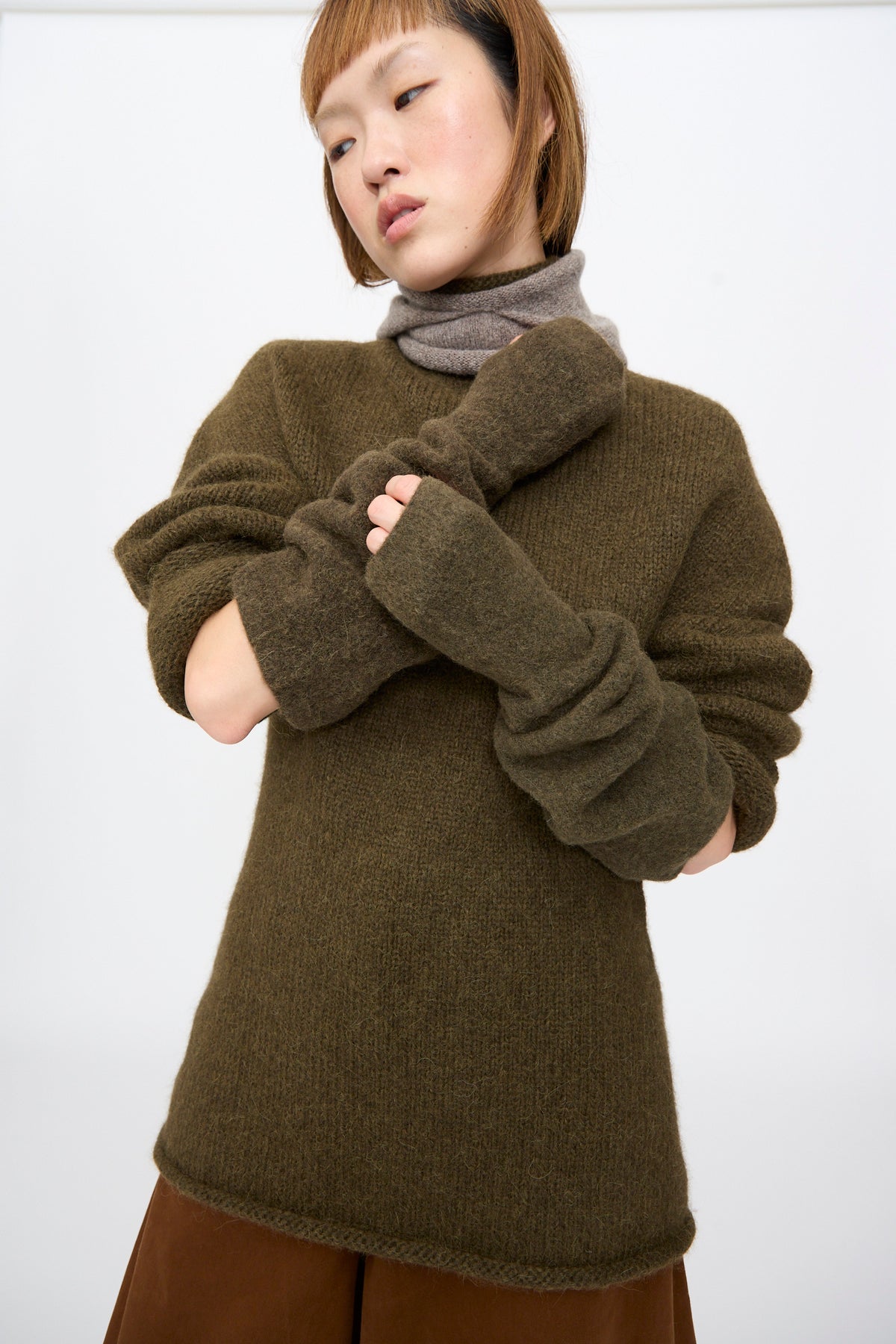 A person wears the Lauren Manoogian Felt Fingerless Gloves in Olive, worn scrunched to the forearm. 