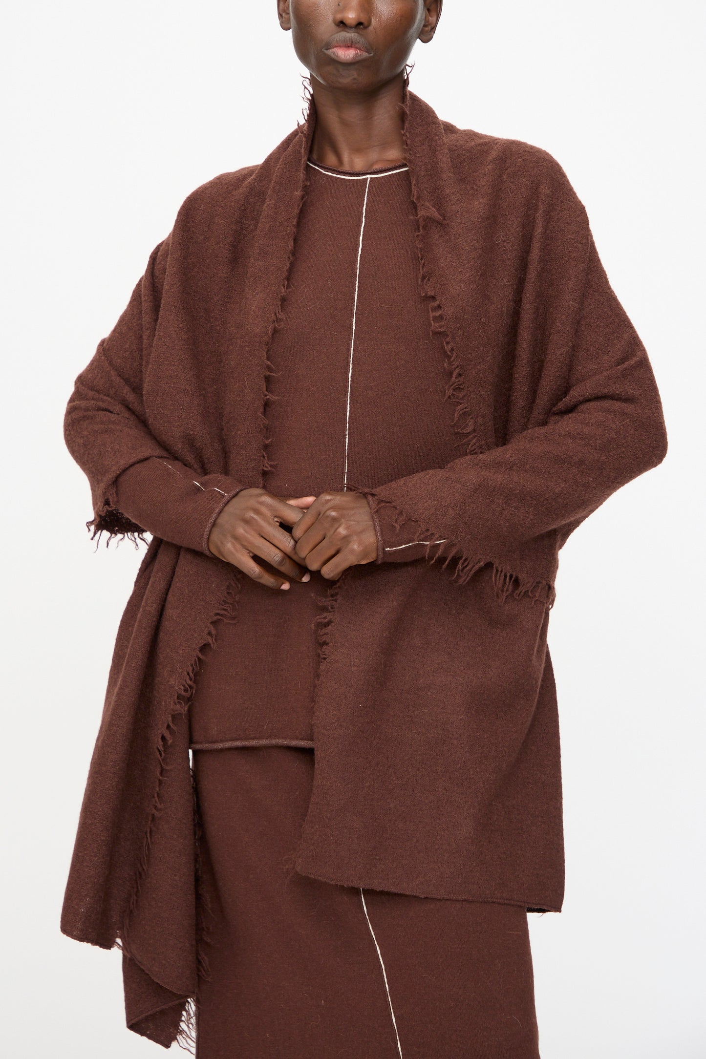 A person wearing the Felt Fringe Scarf in Merlot by Lauren Manoogian over a matching brown outfit with visible white stitching, standing against a plain white background.
