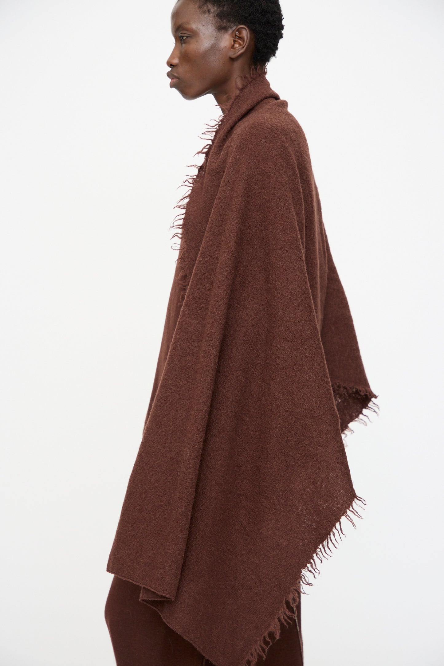 A person stands in profile against a plain white background, wearing the Lauren Manoogian Felt Fringe Scarf in Merlot.