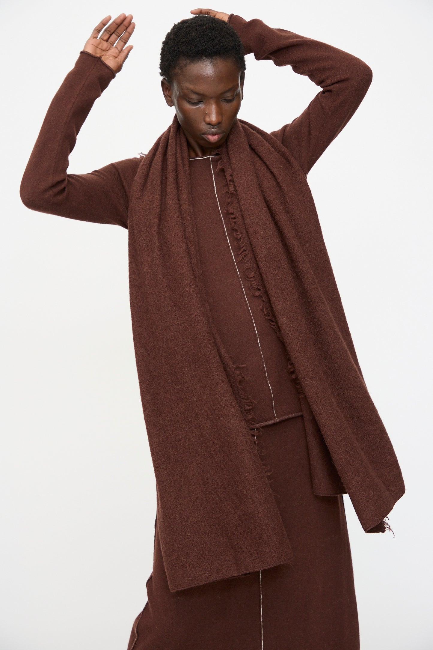 A person wearing the Lauren Manoogian Felt Fringe Scarf in Merlot and a matching brown outfit poses with arms raised against a plain white background.