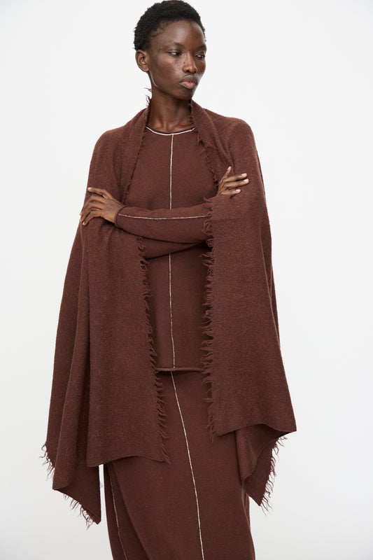A person wearing the Lauren Manoogian Felt Fringe Scarf in Merlot and a matching brown dress with a white vertical seam stands against a plain white background.