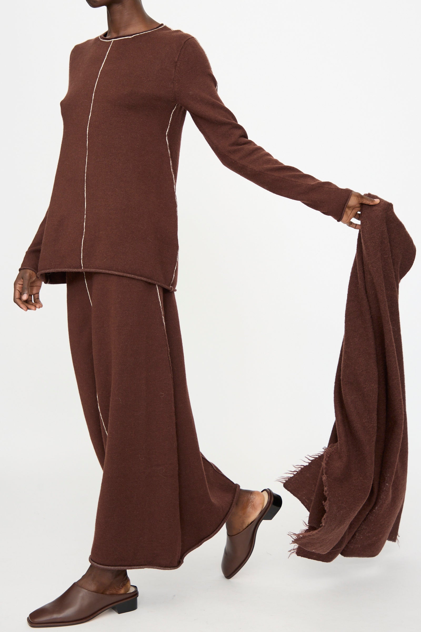 Person wearing a matching brown long-sleeve top and wide-leg pants, holding the Lauren Manoogian Felt Fringe Scarf in Merlot, and wearing brown slip-on shoes against a plain background.