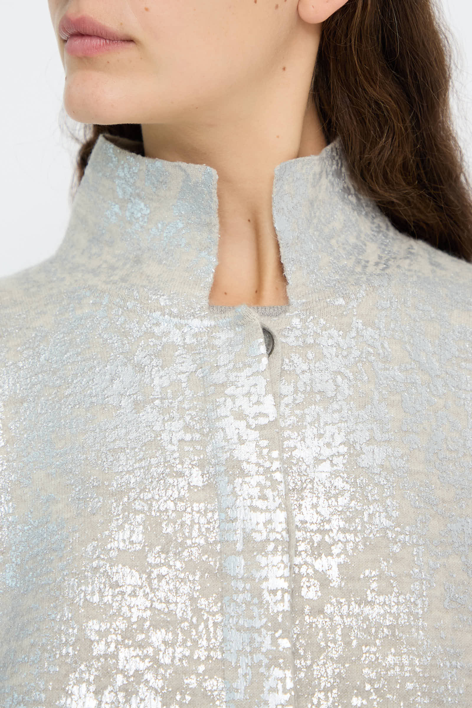 Close-up of a person wearing the Lauren Manoogian Foil Car Coat in Silver Carrara, featuring a relaxed fit with a textured metallic finish, high collar, and a single visible button. Brown hair is partially visible.