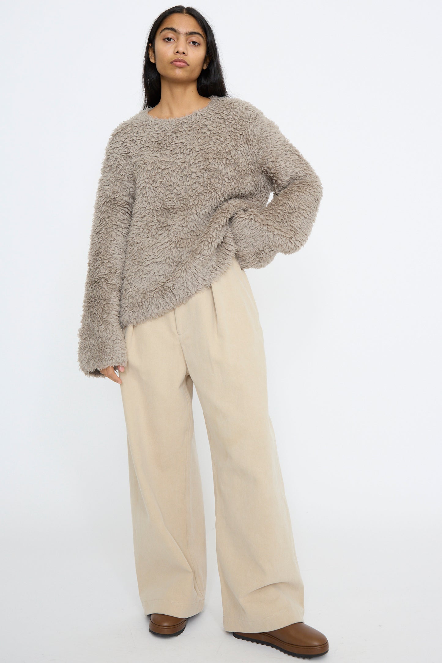 A person wearing a fluffy gray Lauren Manoogian sweater made of Pima cotton, relaxed-fit Frame jeans in khaki, and brown shoes stands against a plain white background.