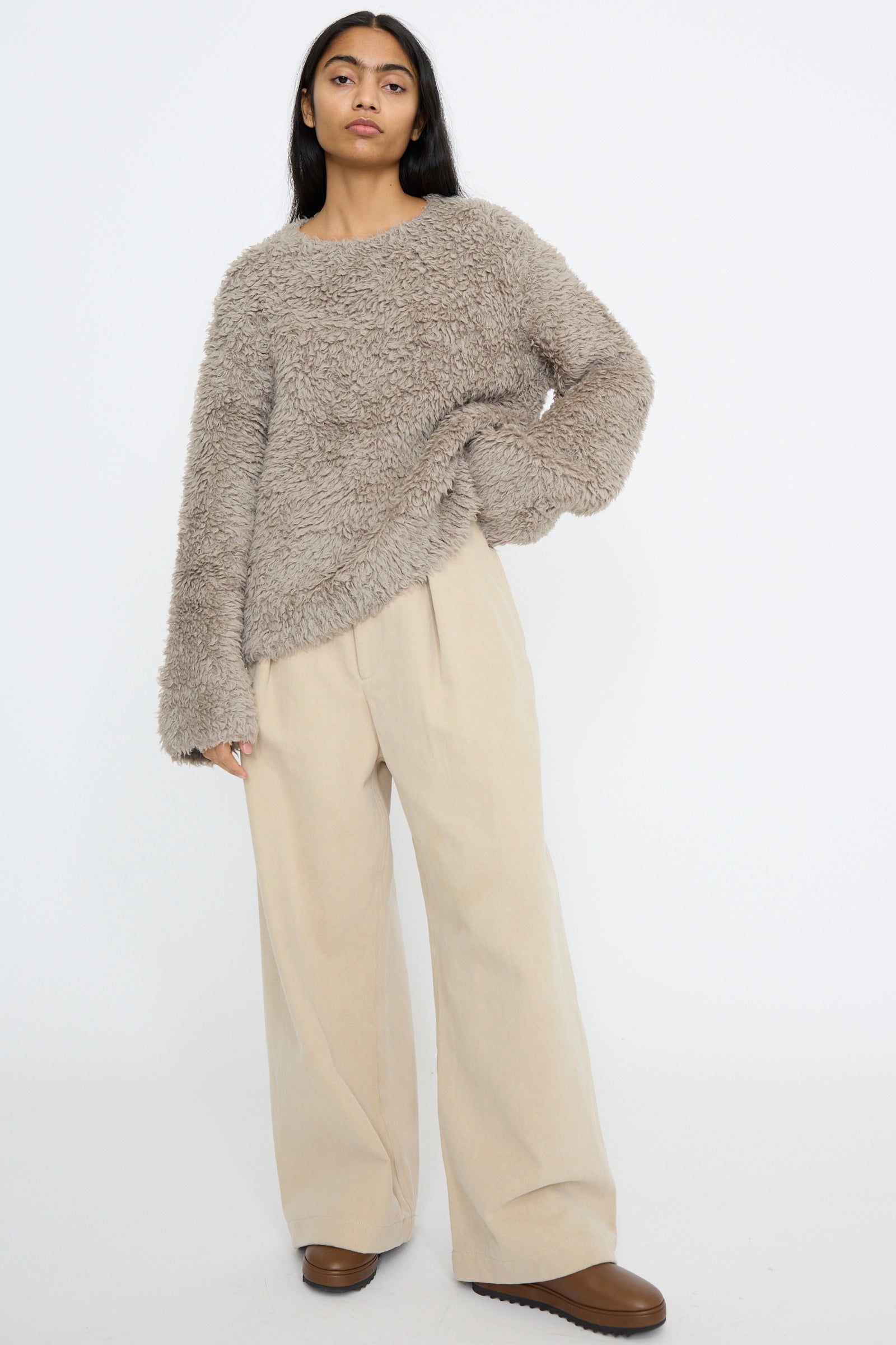 A person wearing a fluffy gray Lauren Manoogian sweater made of Pima cotton, relaxed-fit Frame jeans in khaki, and brown shoes stands against a plain white background.