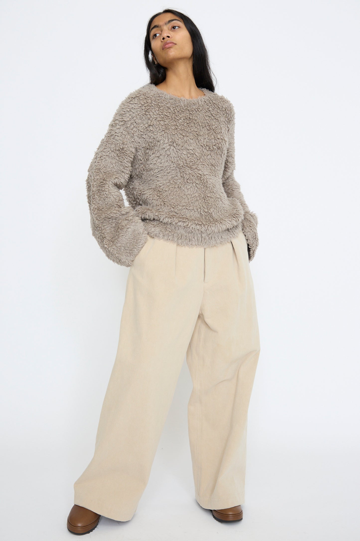 A person wearing a fluffy brown Lauren Manoogian sweater and Frame Jean in Khaki stands against a plain white background.