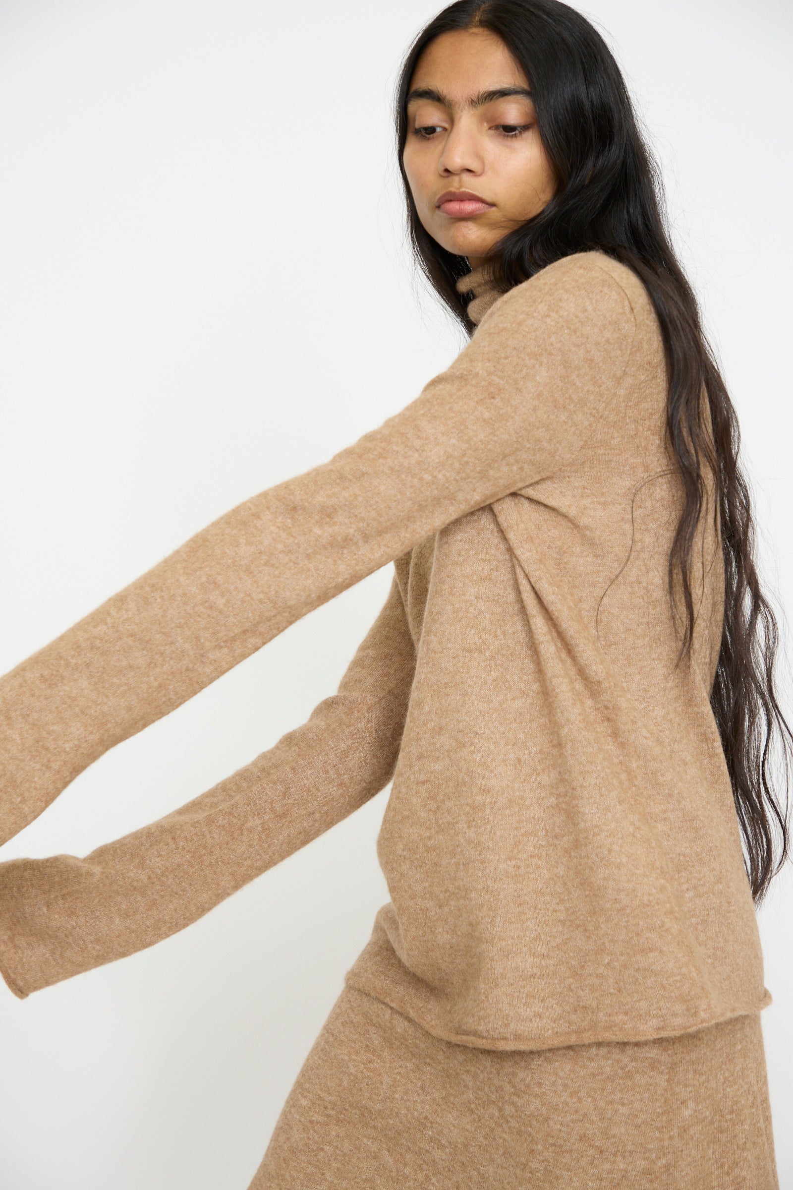 Someone with long hair is wearing the Lauren Manoogian Funnel Turtleneck in Camel, a beige, long-sleeved knit sweater made of soft baby alpaca, featuring a cozy turtleneck, set against a plain background.