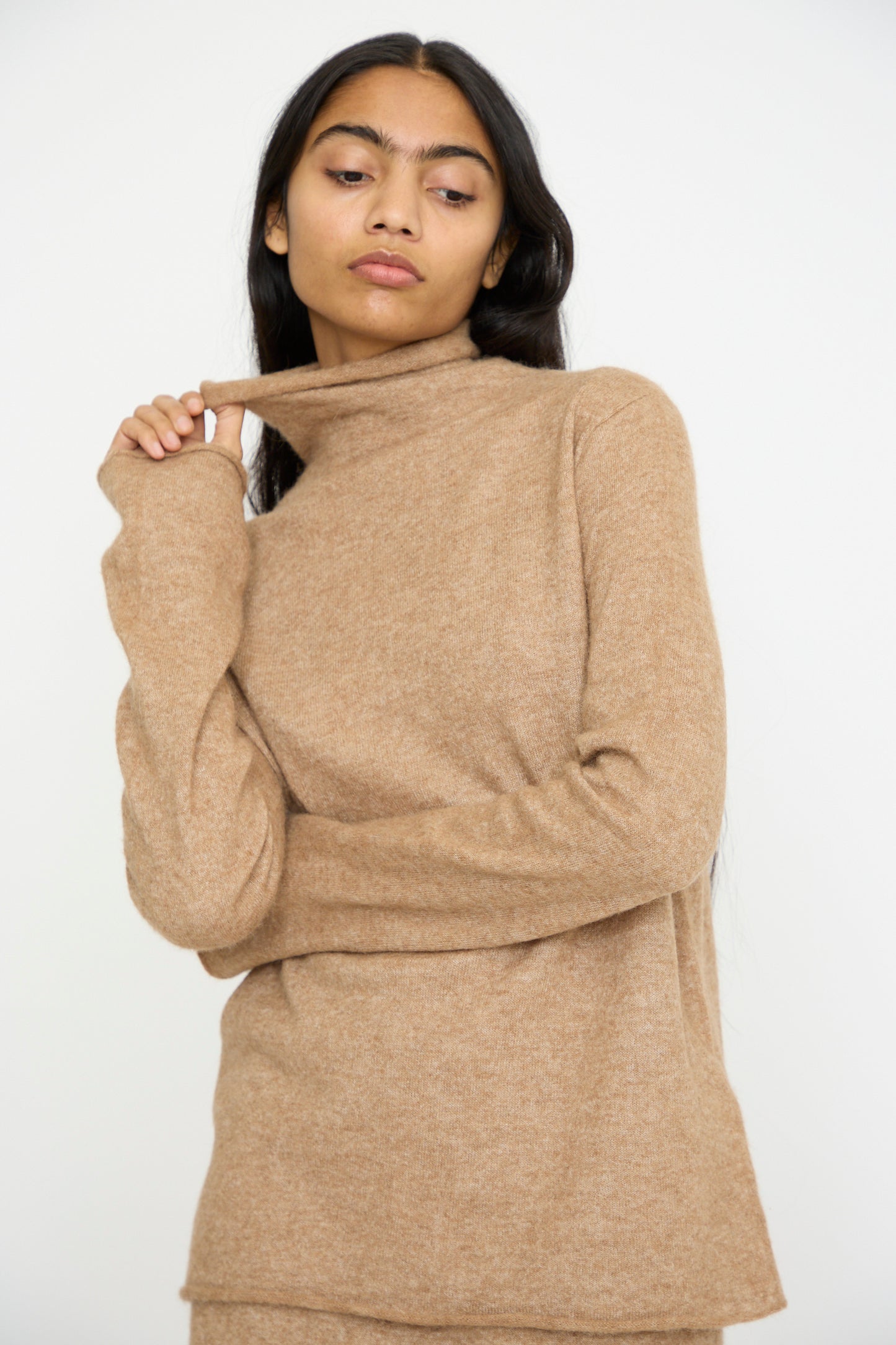 A person dons the Funnel Turtleneck in Camel by Lauren Manoogian, crafted from baby alpaca wool, while looking to the side with a neutral expression.