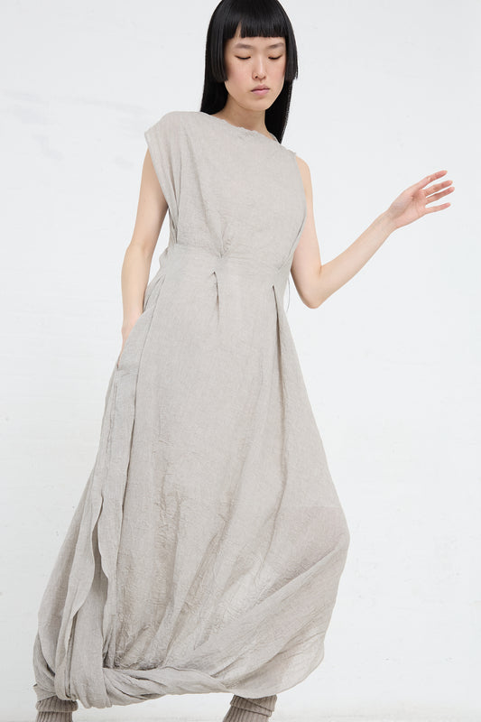 Asian woman in a stylish, draping beige Gauze Twist Dress in Ash made from a cotton/linen blend, standing against a white background by Lauren Manoogian.