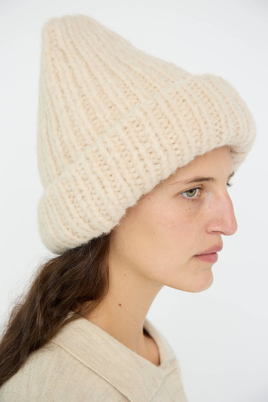 Side profile of a person wearing the Handknit Big Hat in Alabaster by Lauren Manoogian and a beige top against a plain background.