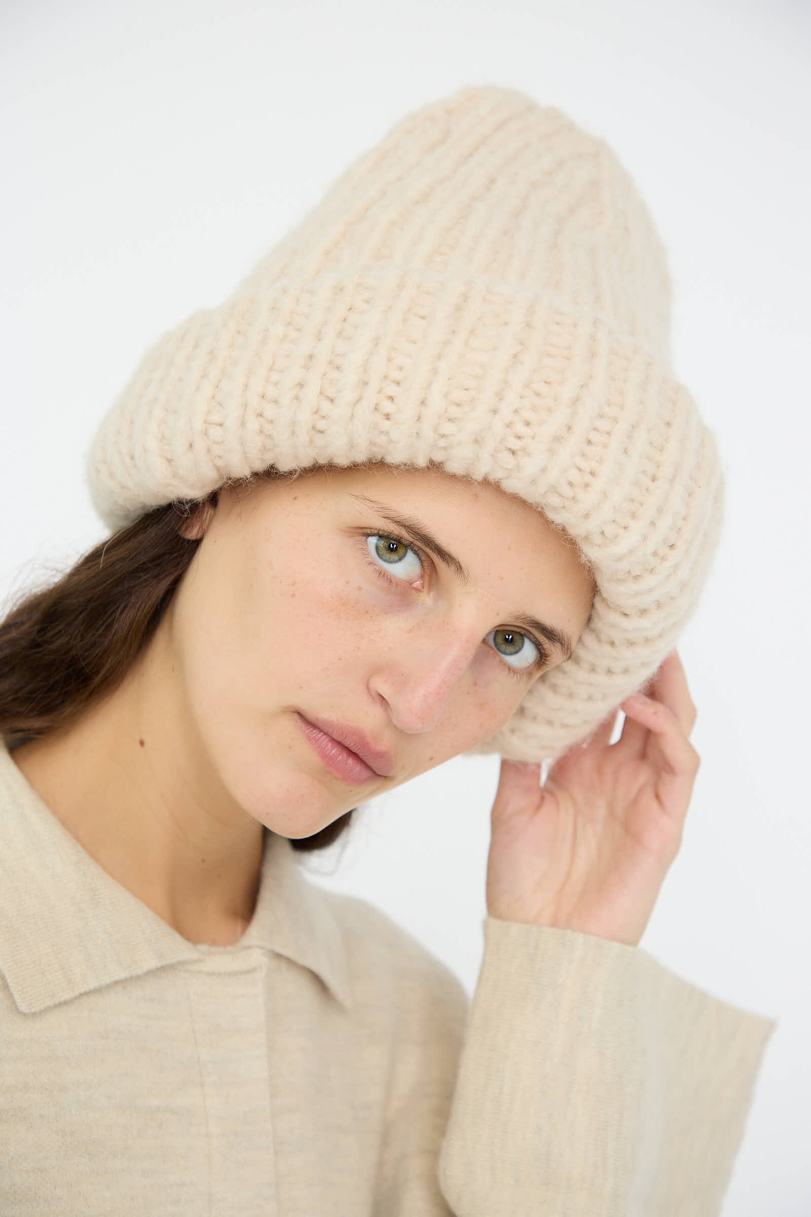 A person wearing the Handknit Big Hat in Alabaster by Lauren Manoogian and a matching sweater, looking at the camera with a neutral expression.