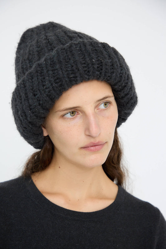 A person is wearing the Lauren Manoogian Handknit Big Hat in Ink, crafted in Peru from an alpaca/wool blend, and a matching dark sweater, looking to the side against a plain background.