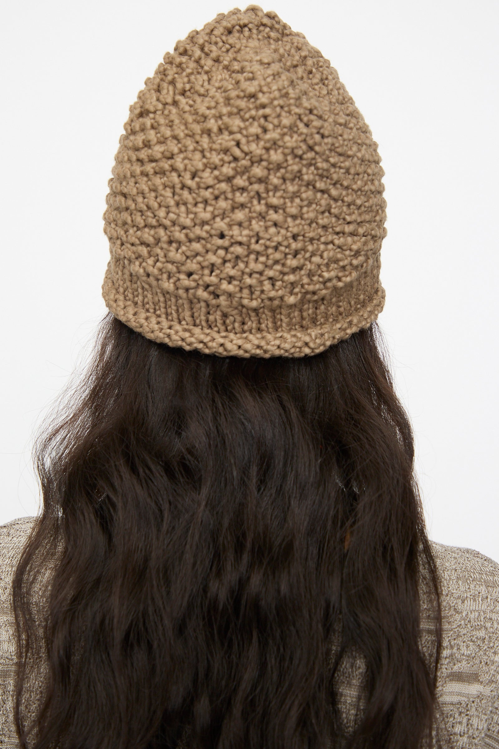 Person with long, wavy dark hair photographed from behind wears the Lauren Manoogian Handknit Crepe Hat in Bark against a plain background.