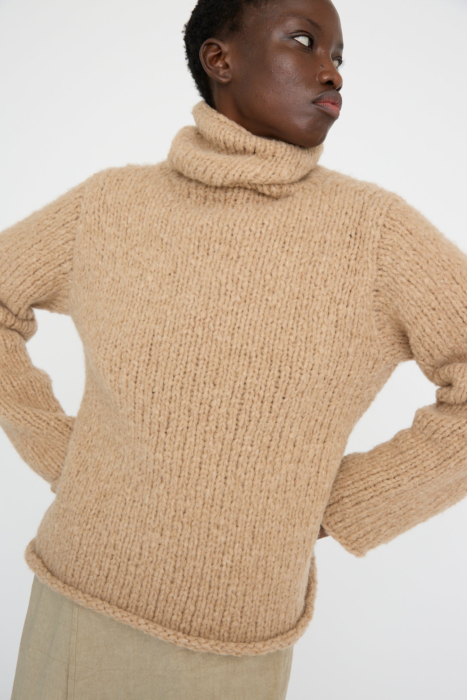 Wearing a Lauren Manoogian Handknit Funnel Sweater in Camel, a person gazes  to the side against a plain background.