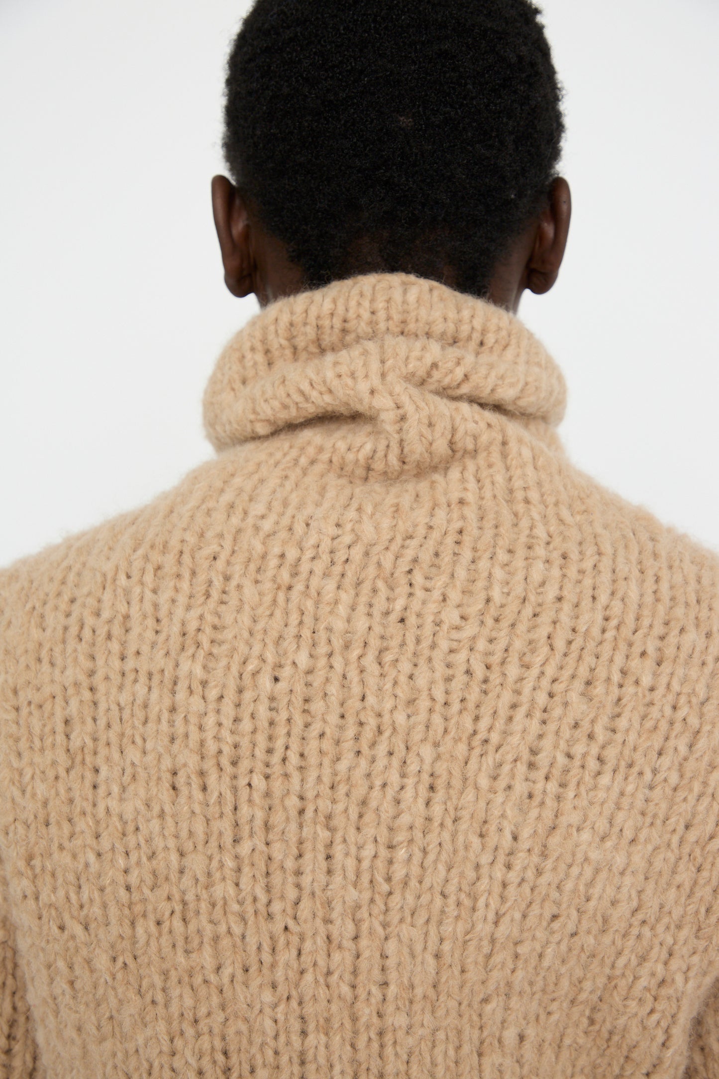 A person wearing a Lauren Manoogian Handknit Funnel Sweater in Camel is seen from the back against a plain background.