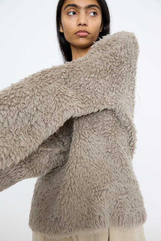 A person stands against a plain white background, wrapped in Lauren Manoogian's Handknit Fur Crewneck in Taupe, made from an oversized alpaca wool blend.