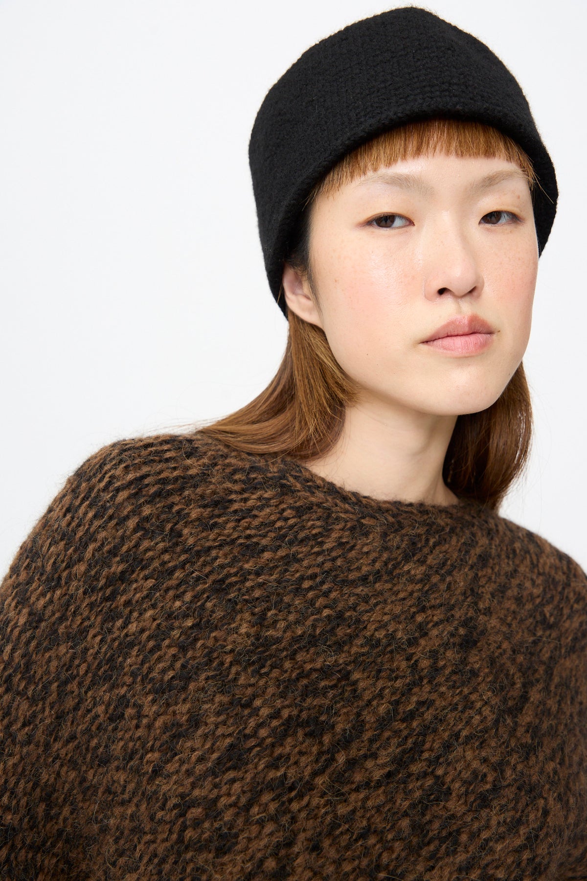 A person wearing a relaxed fit, chunky knit Handknit Manta Pullover in Rust Marl and a black hat.