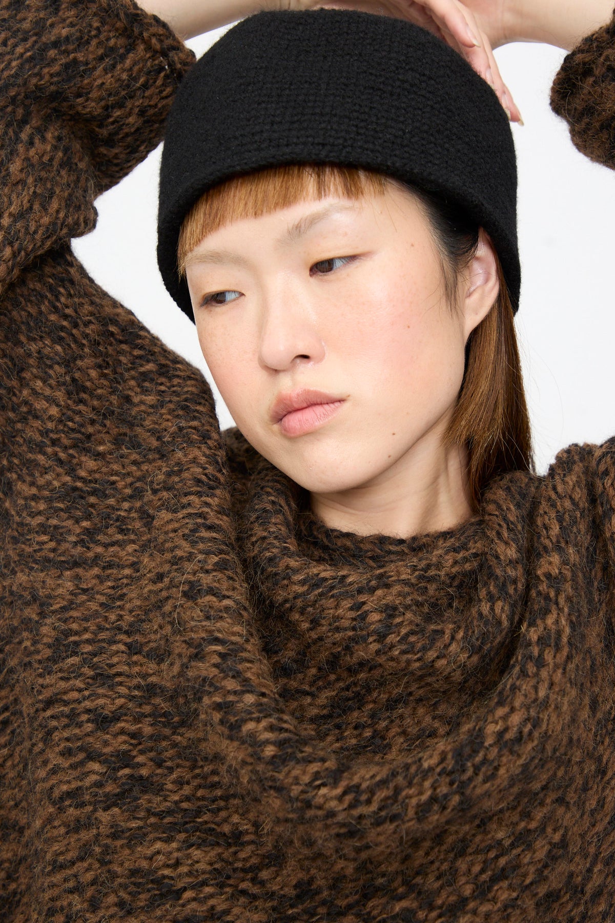 A person wearing a relaxed fit, chunky knit Lauren Manoogian Handknit Manta Pullover in Rust Marl and a black hat.