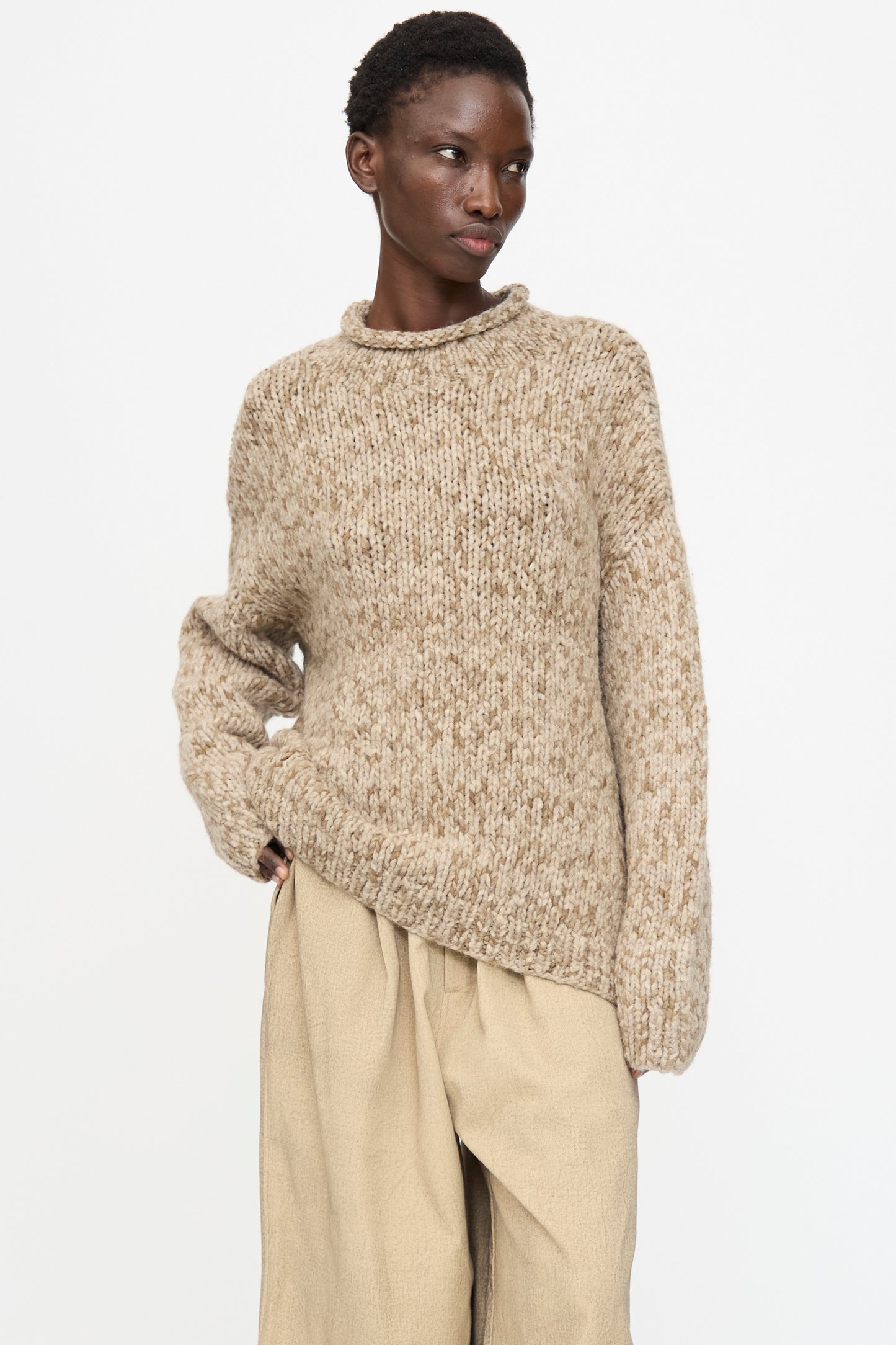 A person wears the Lauren Manoogian Handknit Paint Rollneck in Tobacco with loose light tan pants, standing against a plain white background.