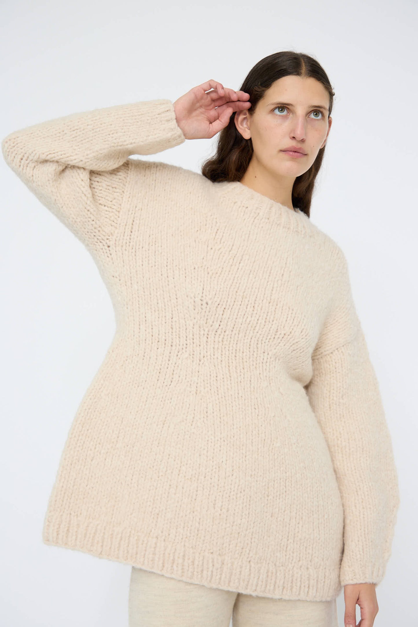 A woman wearing the Lauren Manoogian Handknit Peplum Pullover in Alabaster saluting gracefully with her hand.