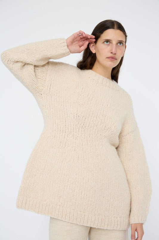 A woman wearing the Lauren Manoogian Handknit Peplum Pullover in Alabaster saluting gracefully with her hand.