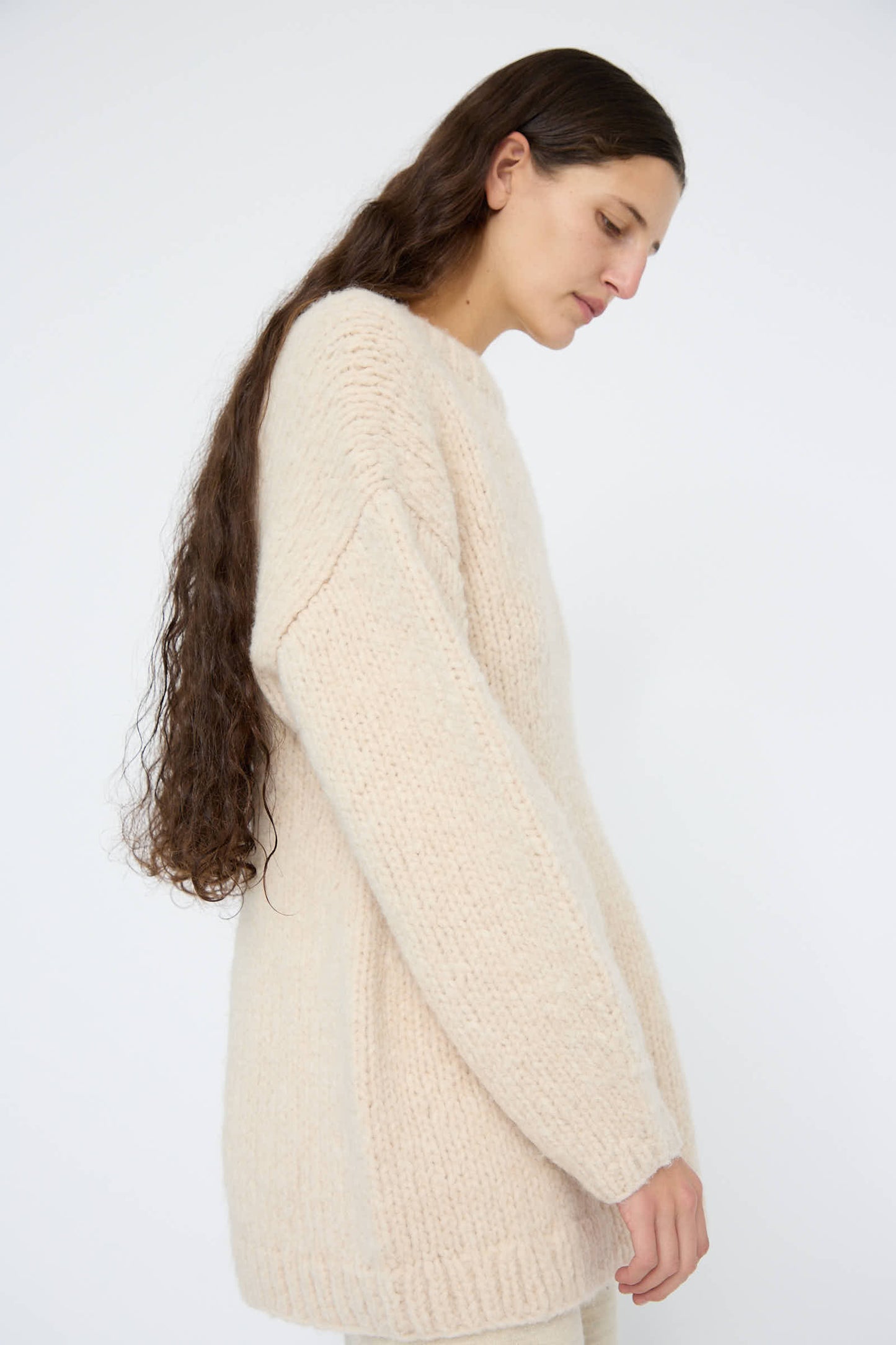 A person with long hair wearing the Handknit Peplum Pullover in Alabaster by Lauren Manoogian, crafted from luxurious baby alpaca, stands against a plain white background.