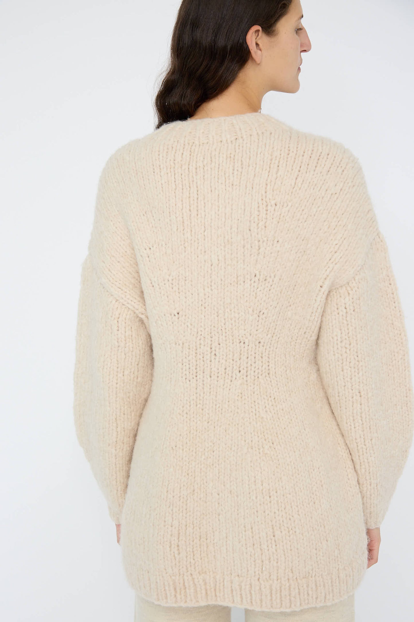 A person facing away is wearing the Handknit Peplum Pullover in Alabaster, crafted by Lauren Manoogian with luxurious baby alpaca and featuring long sleeves.