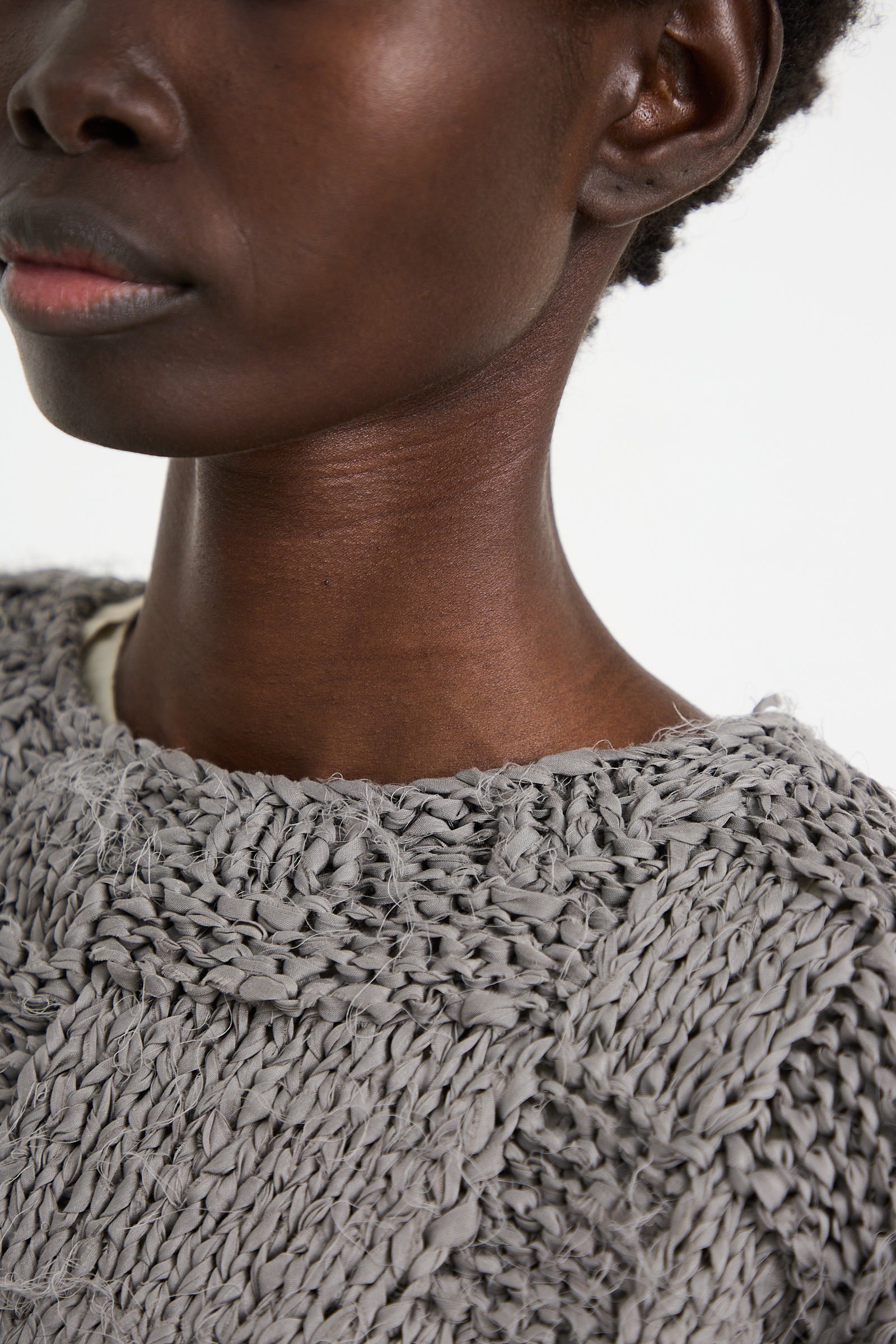 Close-up of a person wearing a Lauren Manoogian Handknit Pullover Sweater in Gris. Only the lower face, neck, and upper chest are visible, showcasing the textured pattern and highlighting the relaxed fit of the knitted garment.