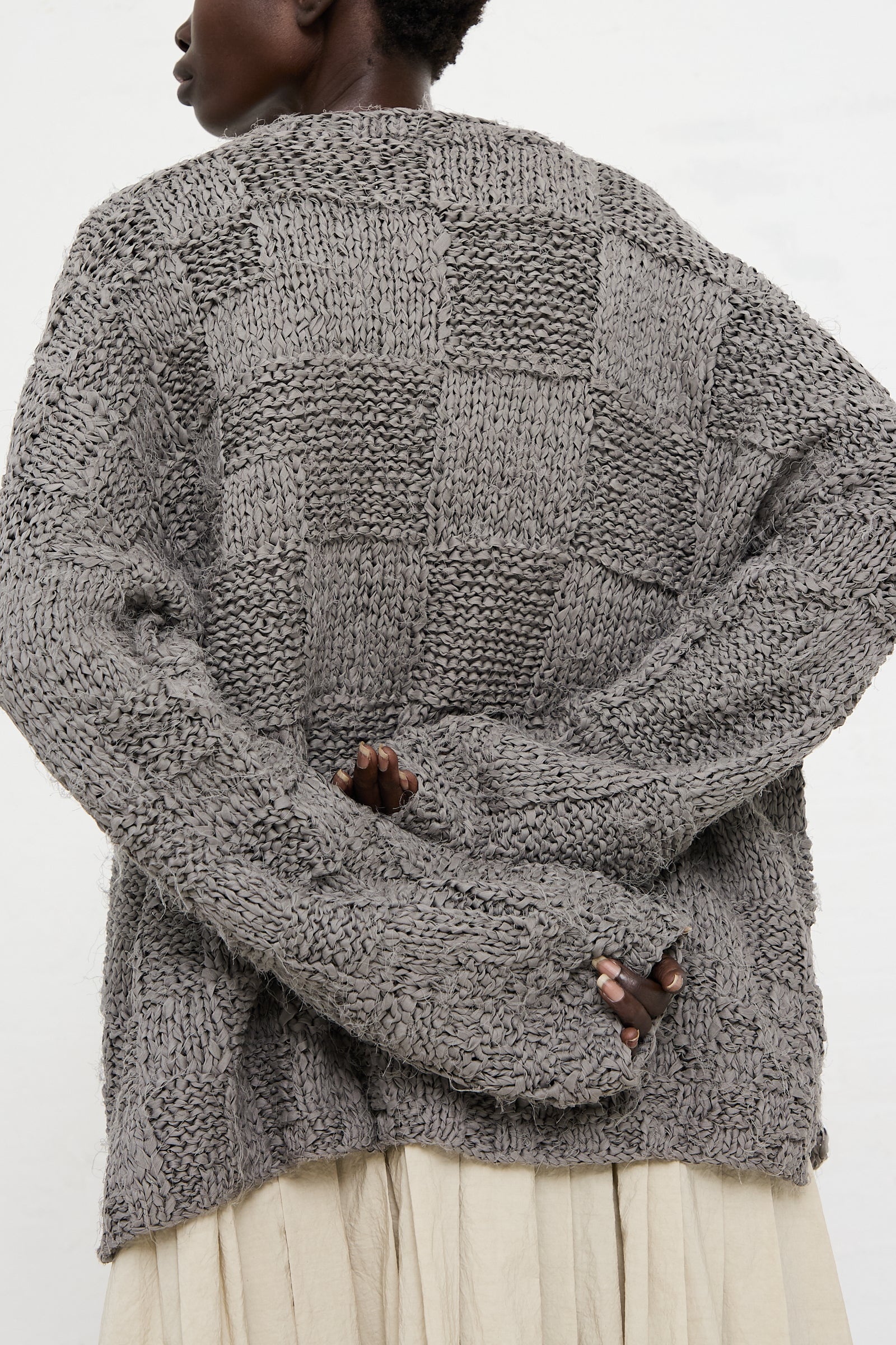A person wearing a Lauren Manoogian Handknit Pullover Sweater in Gris stands with hands clasped behind their back.