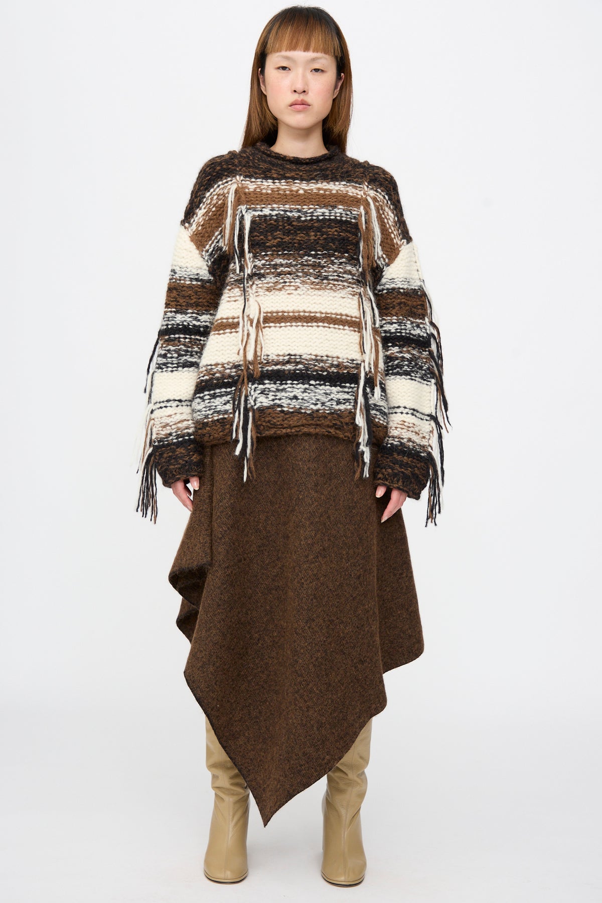A model wearing a Lauren Manoogian Handknit Rio Rollneck in Marl Stripe, styled with a brown asymmetrical skirt and tan boots.