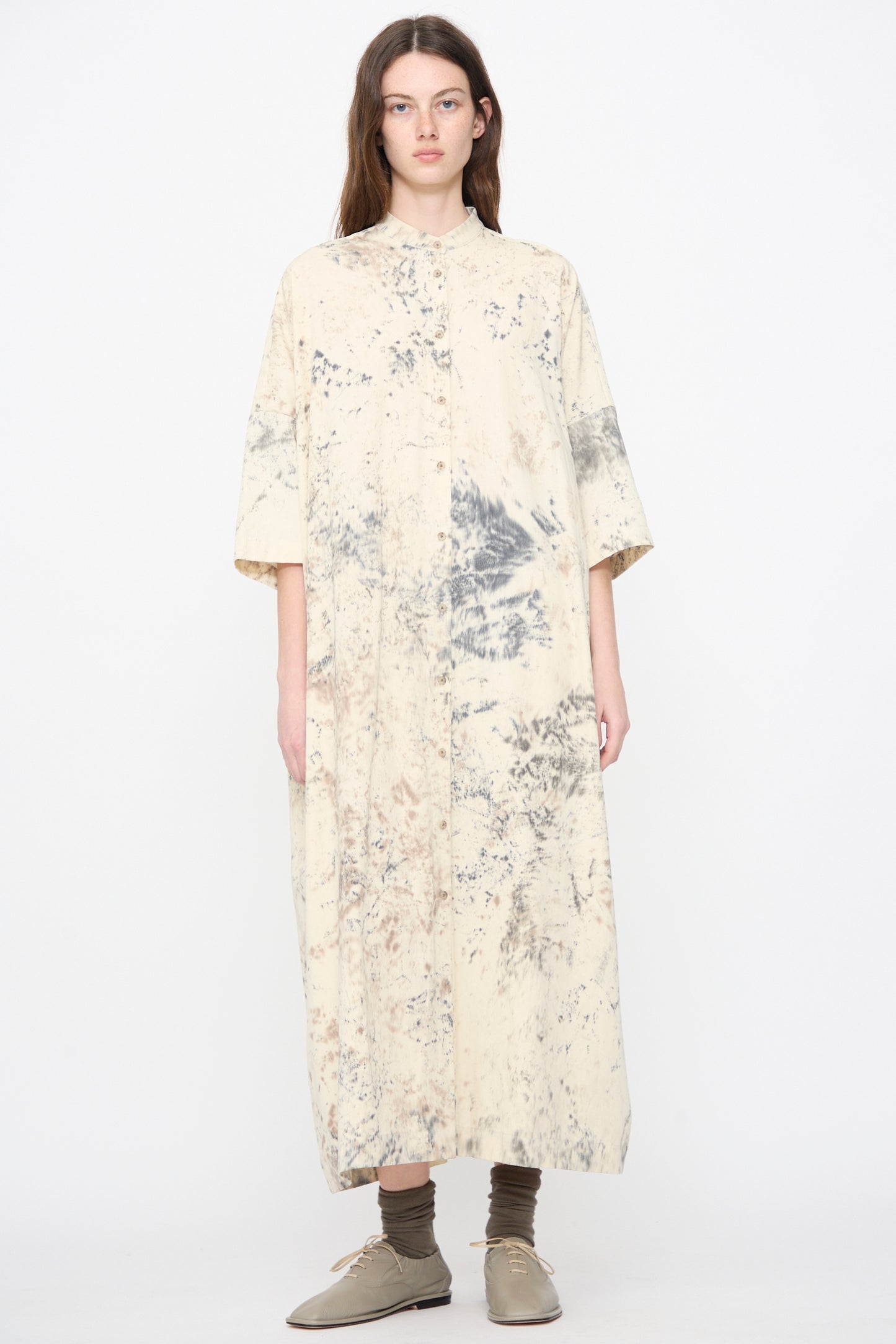 A woman wearing the Lauren Manoogian Handpaint Shirt Dress in Natural, featuring a marble-inspired pattern, paired with brown socks and grey shoes.