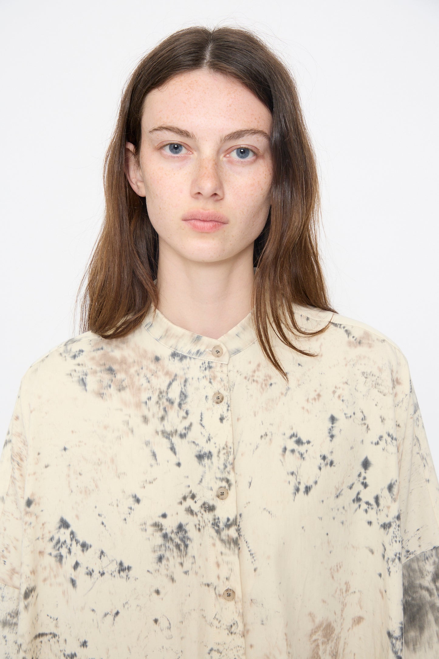 A woman with straight brown hair wears the Lauren Manoogian Handpaint Shirt Dress in Natural, featuring a black and brown abstract pattern, standing facing the camera against a plain white background.