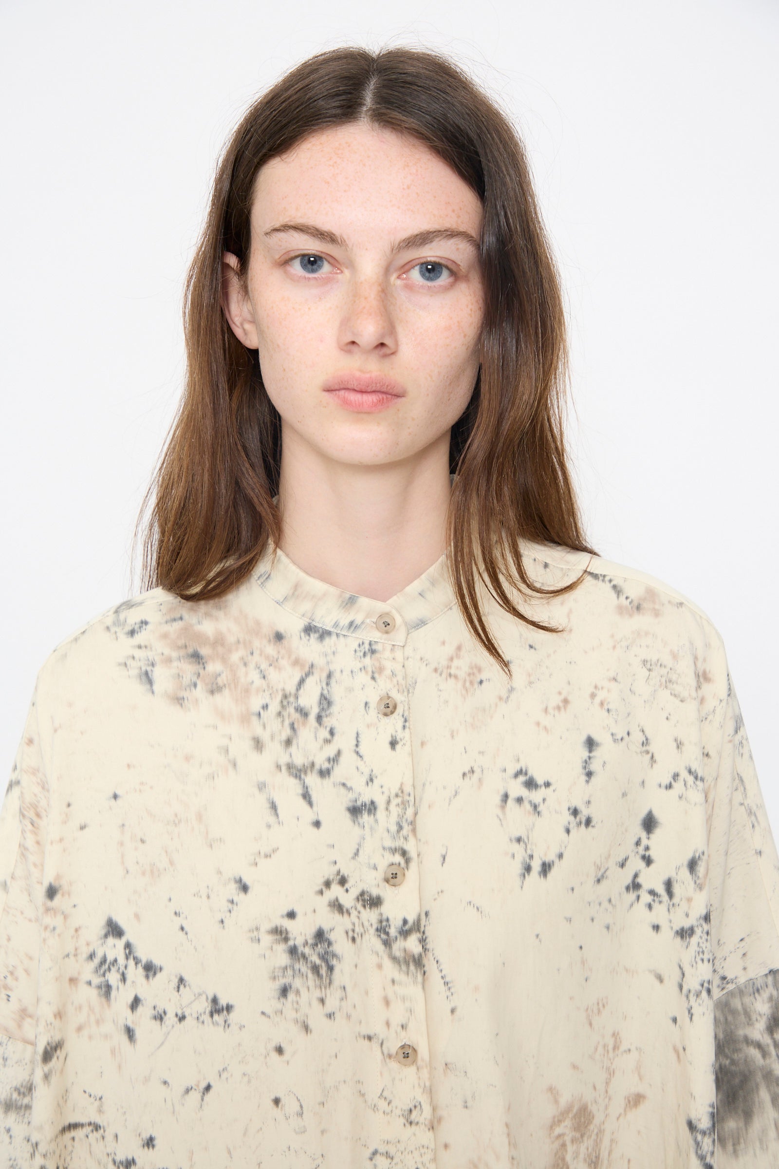 A woman with straight brown hair wears the Lauren Manoogian Handpaint Shirt Dress in Natural, featuring a black and brown abstract pattern, standing facing the camera against a plain white background.