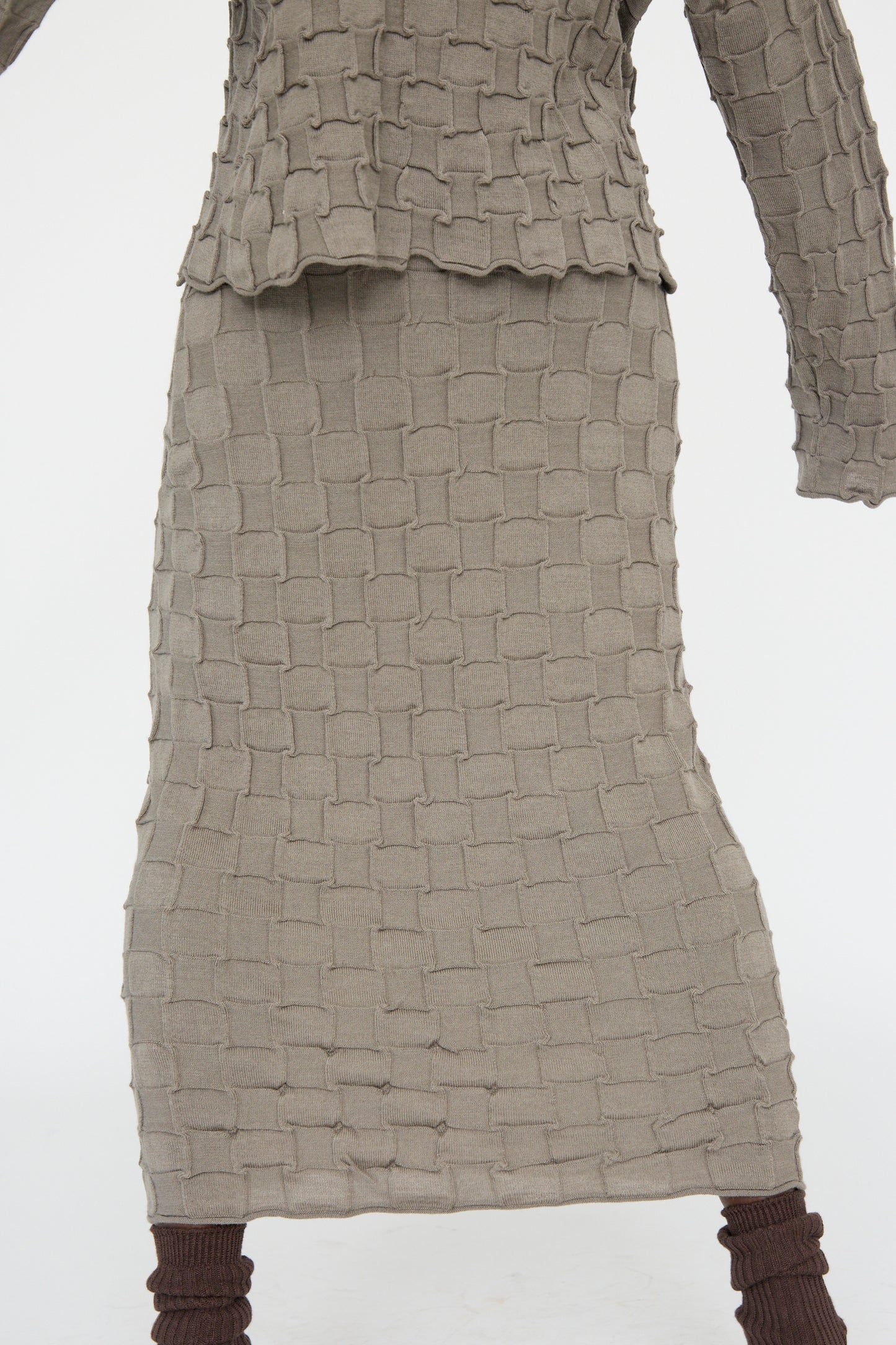 A person is elegantly dressed in a textured, soft merino wool outfit by Lauren Manoogian, featuring a matching top and the Inlay Skirt in Concrete with a grid-like pattern.