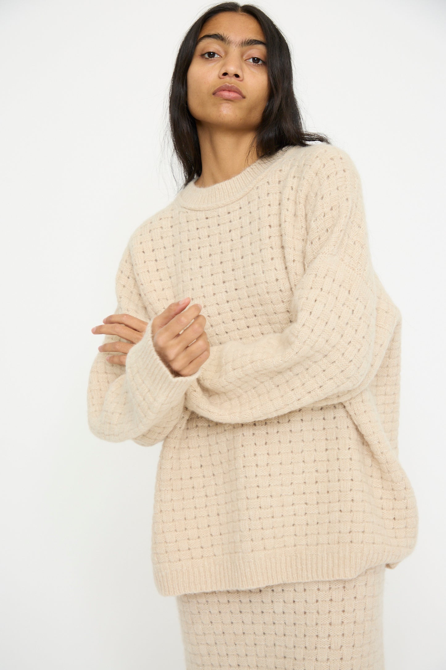 A person wears the Lauren Manoogian Interlace Crewneck in Alabaster and a matching skirt made from an alpaca wool blend, standing against a plain white background.