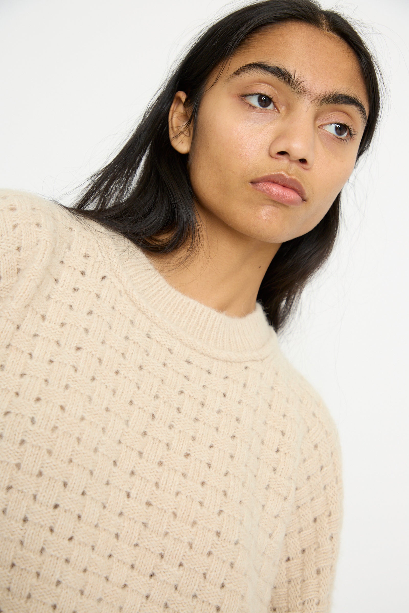 A person with long dark hair wears the oversized Interlace Crewneck in Alabaster by Lauren Manoogian, crafted from a cozy alpaca wool blend, against a neutral background.