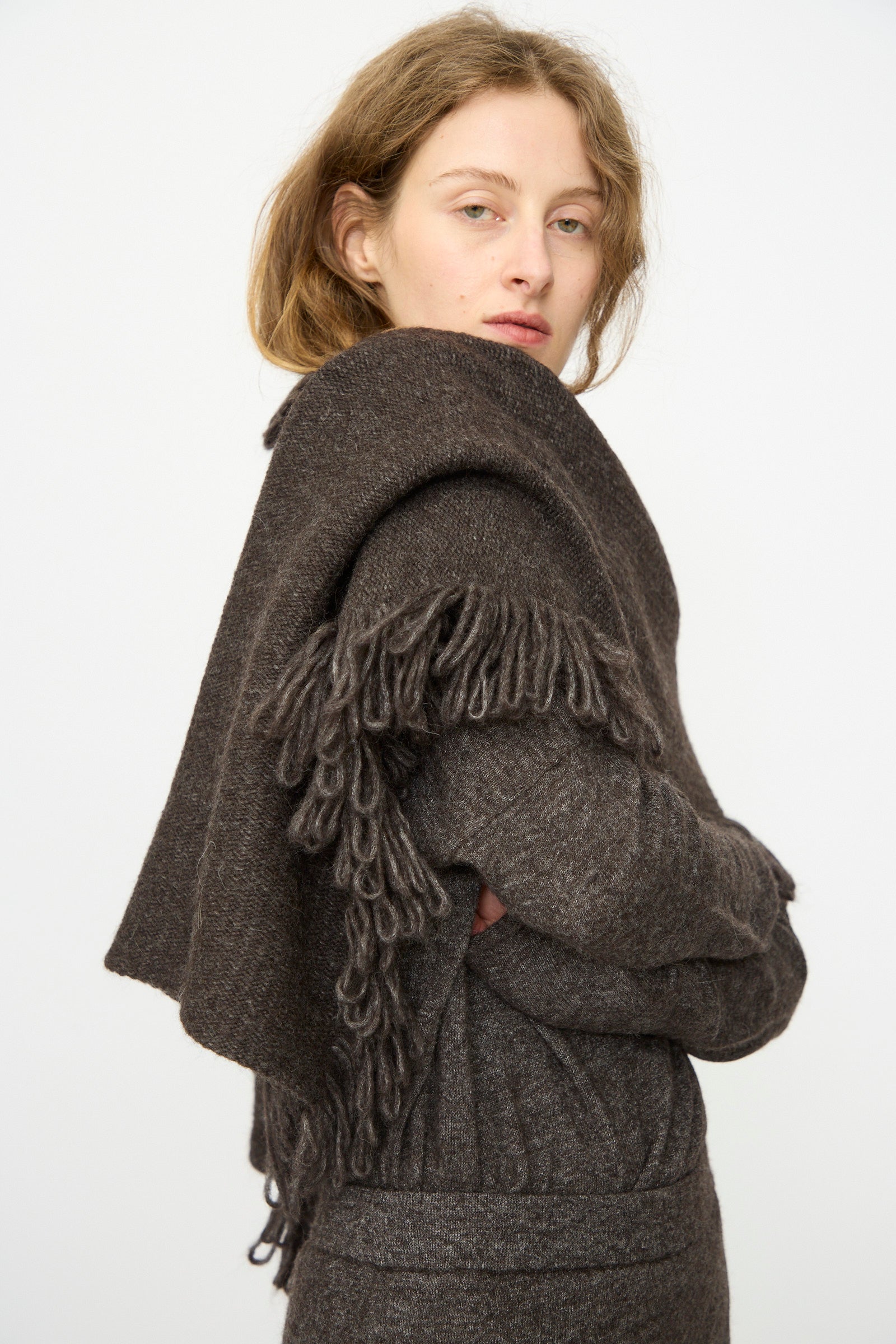 A person with light brown hair wears the Lauren Manoogian Knitweave Wrap in Blackened, paired with a dark brown knit outfit, standing against a plain white background.