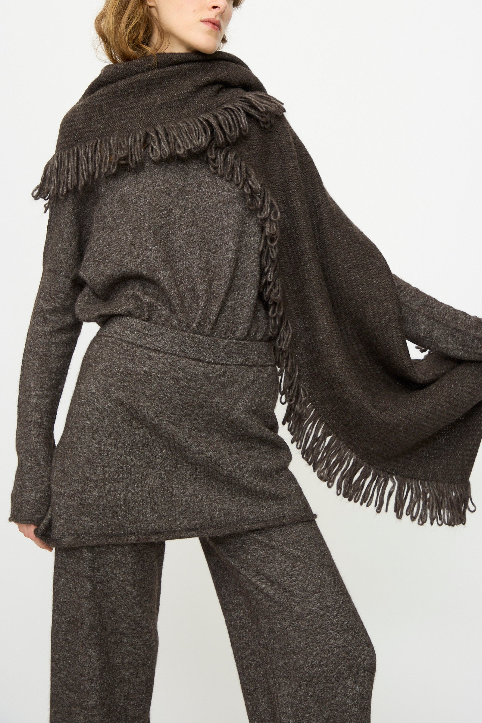 A person wearing a loose-fitting dark brown knit outfit with wide-leg pants and a Lauren Manoogian Knitweave Wrap in Blackened draped over their shoulders.